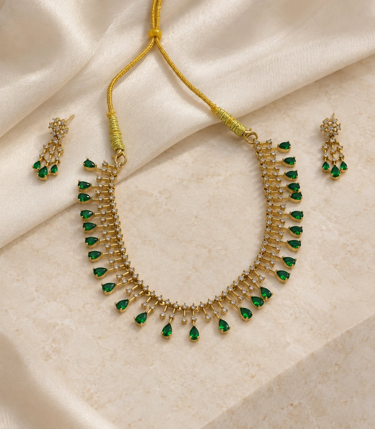Gold-tone emerald-green necklace and matching pair of earrings arranged on a neutral surface #Color_Emerald