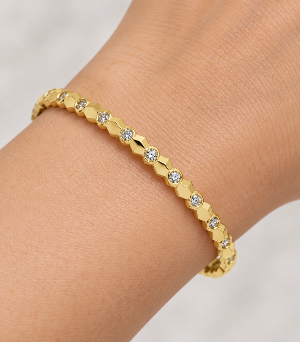 JIMIKI Gold-Tone Faceted Bezel Crystal Bangle — close-up of the bangle worn on the wrist #color_gold-tone / clear
