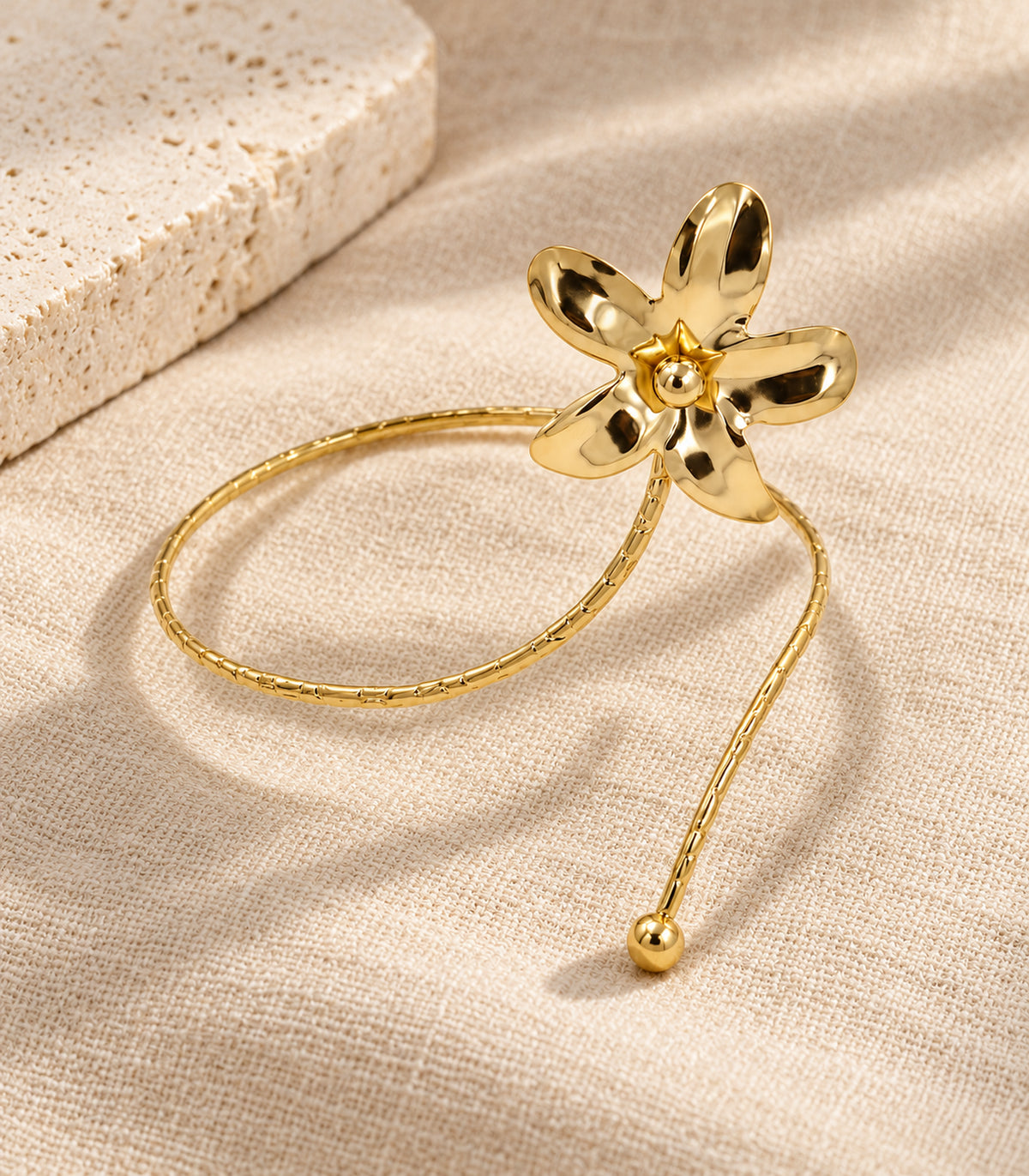 Complete single gold-tone five-petal flower and ball-tip arm cuff arranged on linen