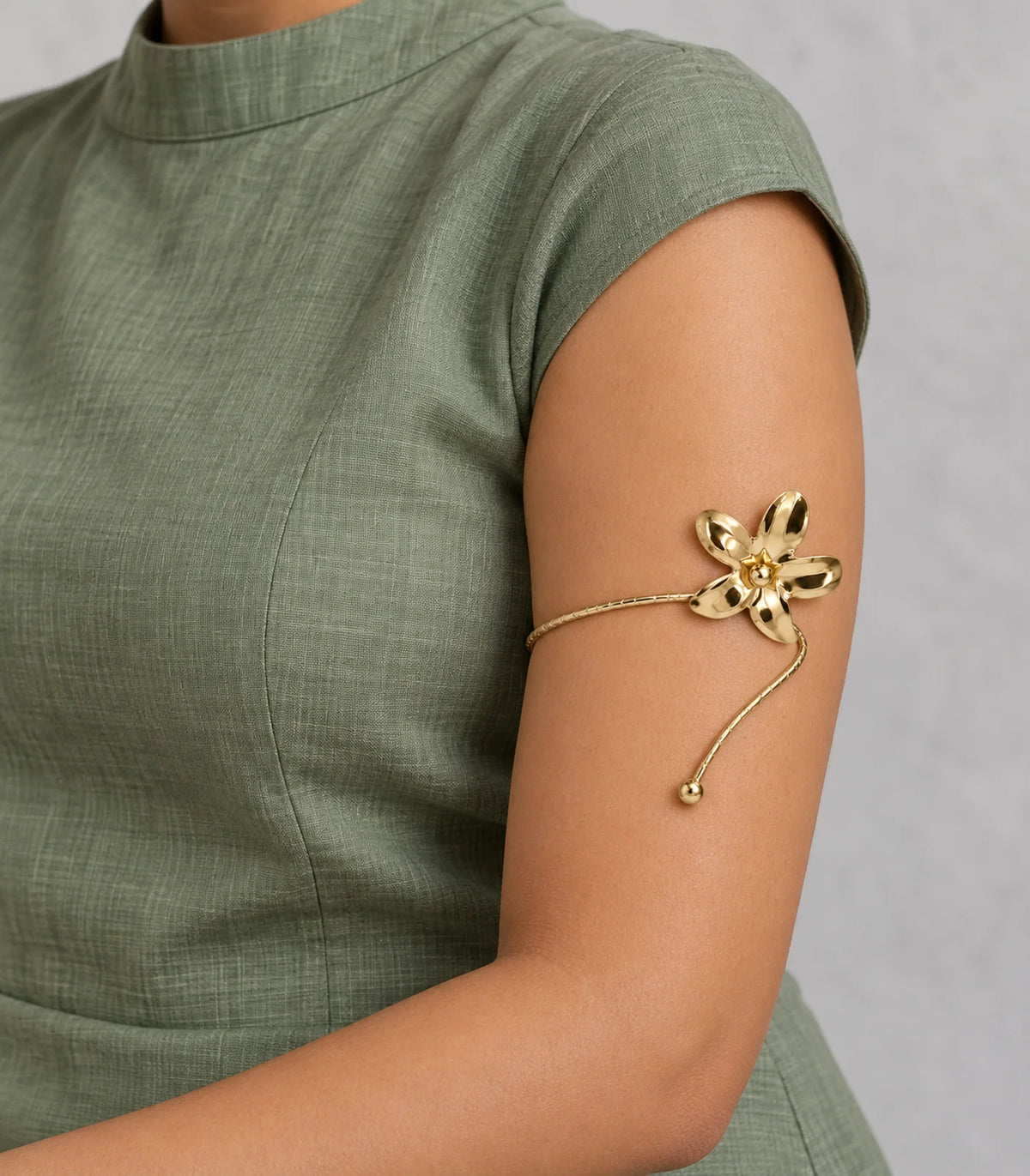 Gold-tone five-petal flower and ball-tip arm cuff worn on the upper arm with sage-green modest clothing