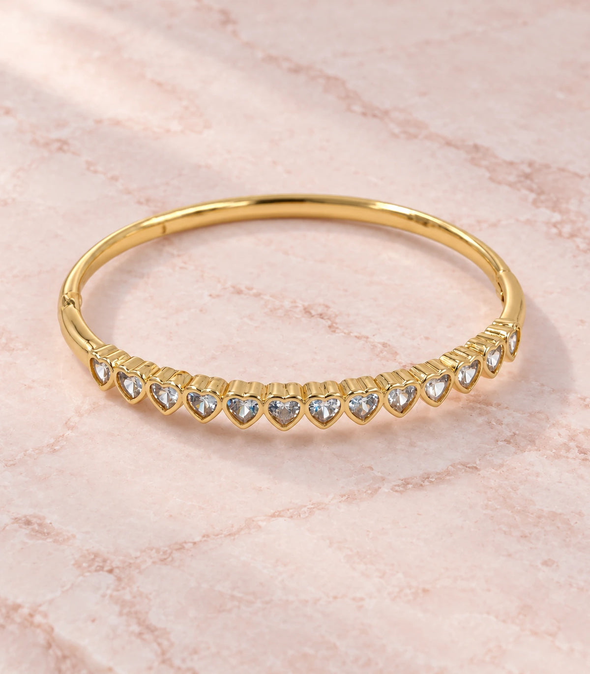 JIMIKI Gold-Tone Graduated Heart Crystal Bangle — bangle in a styled flat lay #color_gold-tone / clear