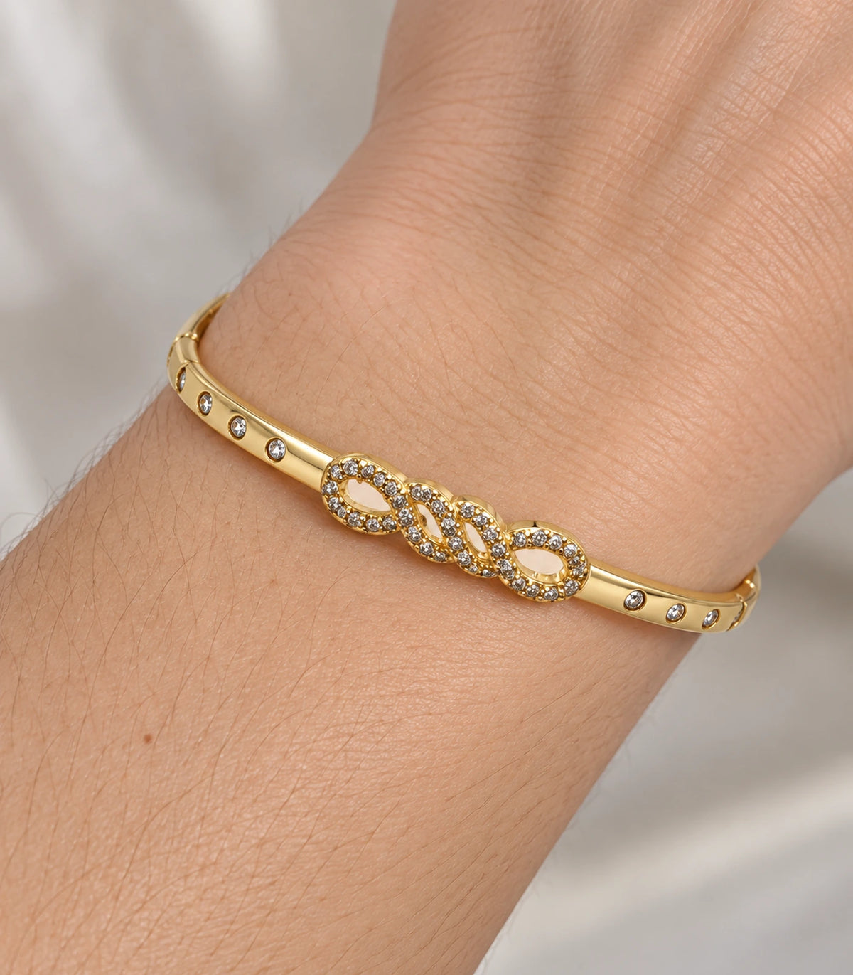 JIMIKI Gold-Tone Infinity Knot Bezel Stone Bangle — close-up of the bangle worn on the wrist #color_gold-tone / clear