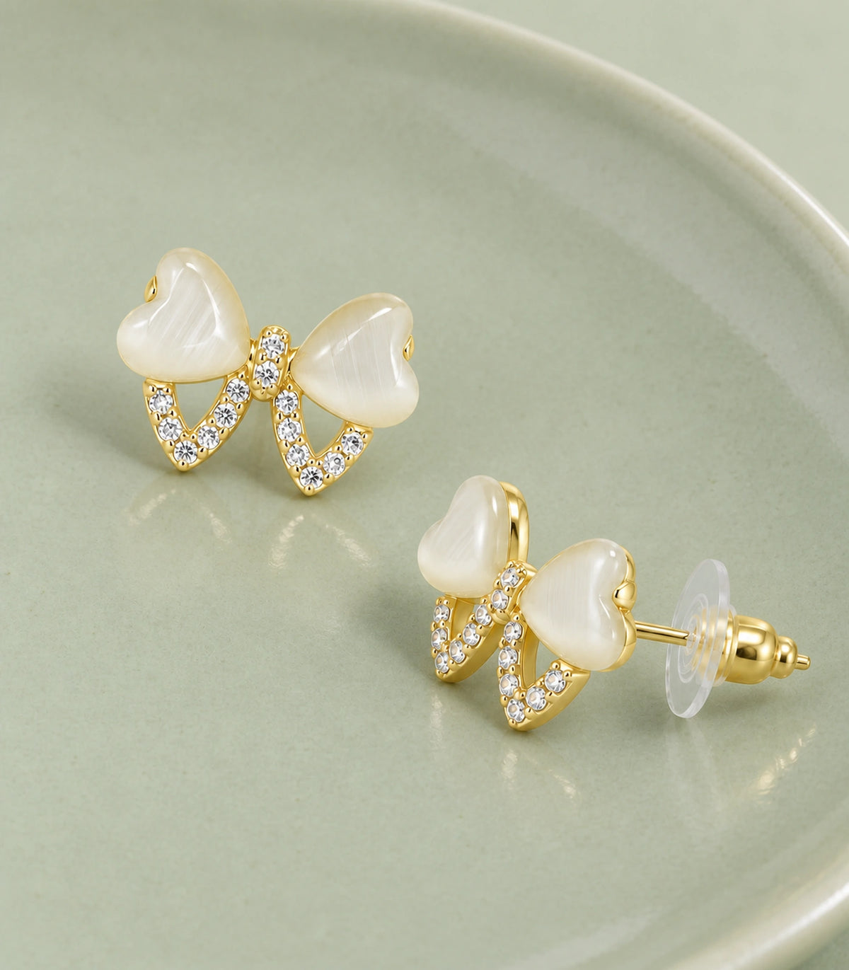 JIMIKI Gold Tone Ivory Heart Bow Crystal Stud Earring Pair in Gold tone, editorial flat lay