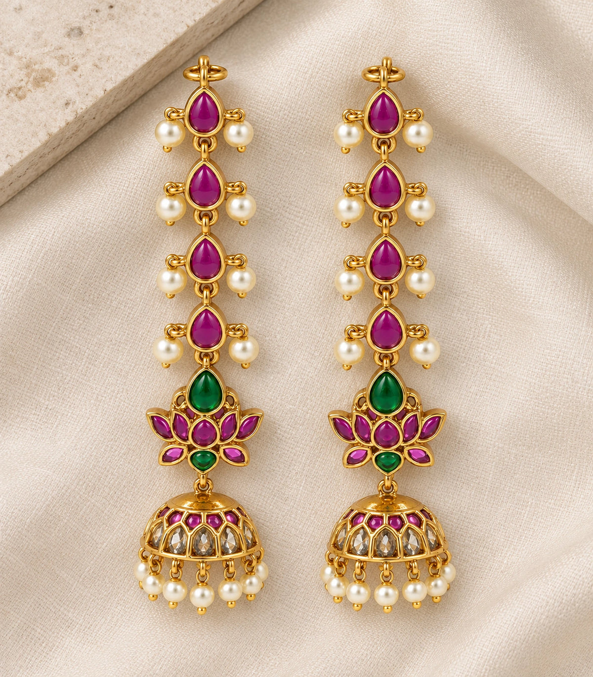 Matching pair of gold-tone magenta and green lotus jhumka earrings on fabric