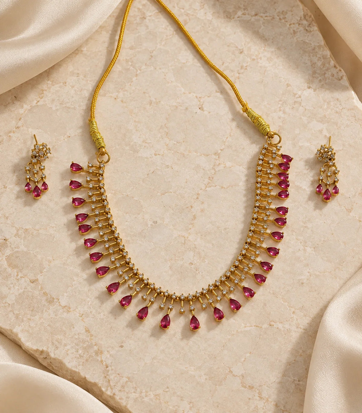 Gold-tone magenta necklace and matching pair of earrings arranged on a neutral surface #Color_Magenta