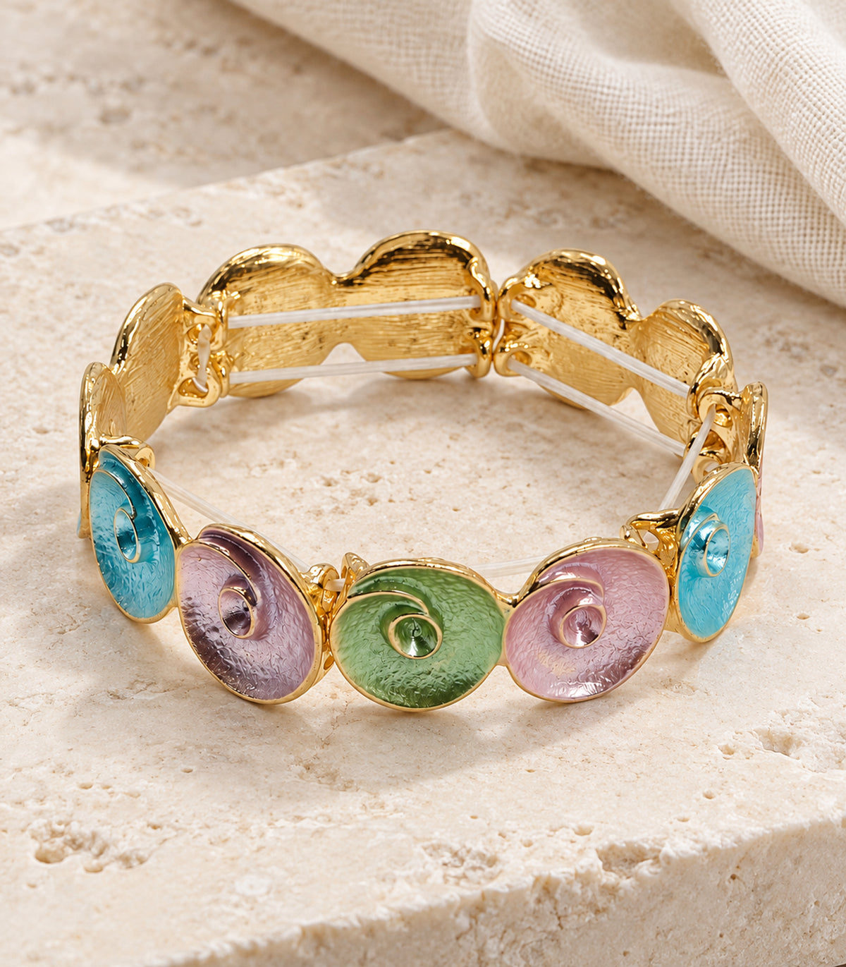 Gold-tone pastel spiral disc bracelet - editorial flatlay view, one bracelet