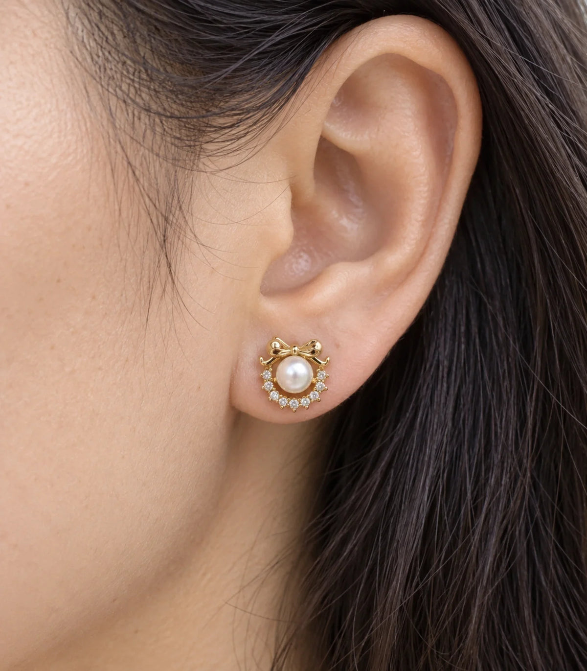 JIMIKI gold-tone pearl wreath bow stud earring worn close-up showing pearl-style centre and curved crystal-style border #color_gold-tone