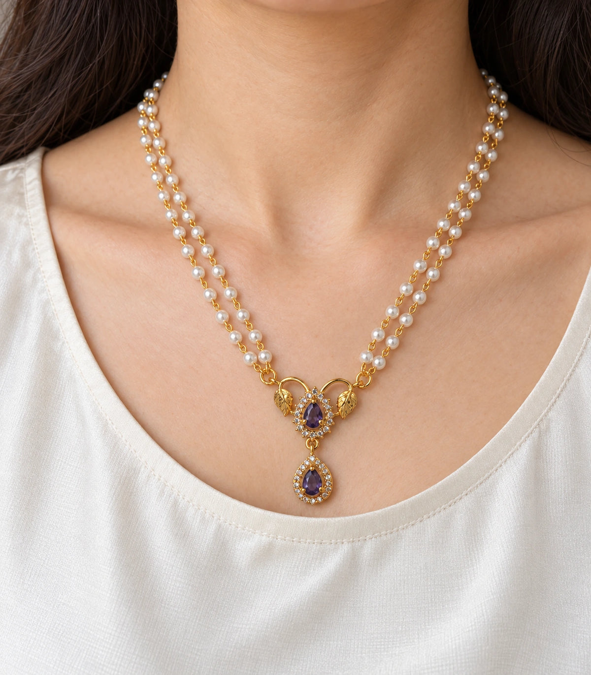 Close view of the single worn purple pendant necklace with two gold leaves, two teardrops and clear-stone surrounds; ears and eyes outside frame.