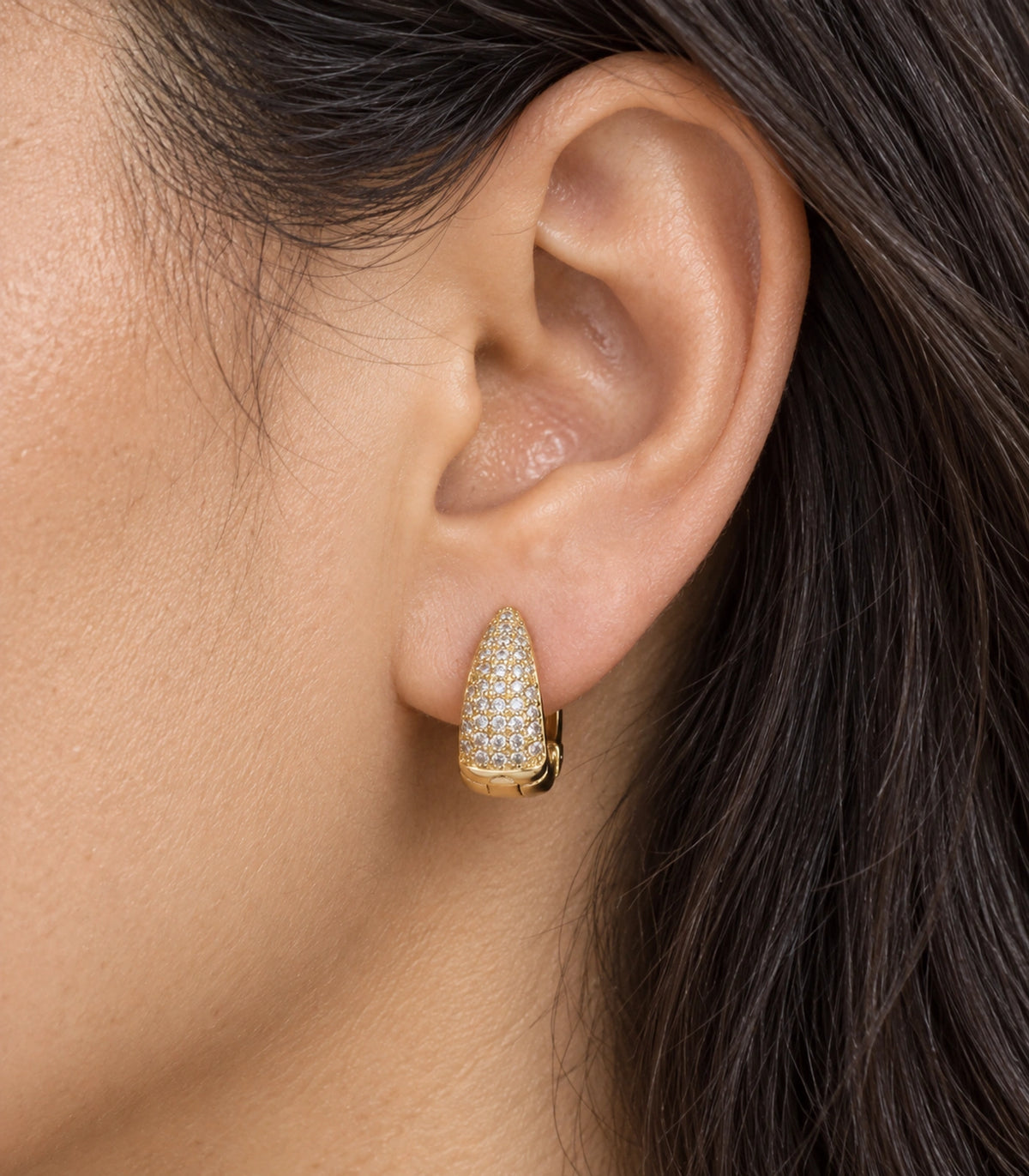 JIMIKI Gold Tone tapered pave huggie hoop earrings, worn closeup of the tapered clear pave front #color_gold-tone
