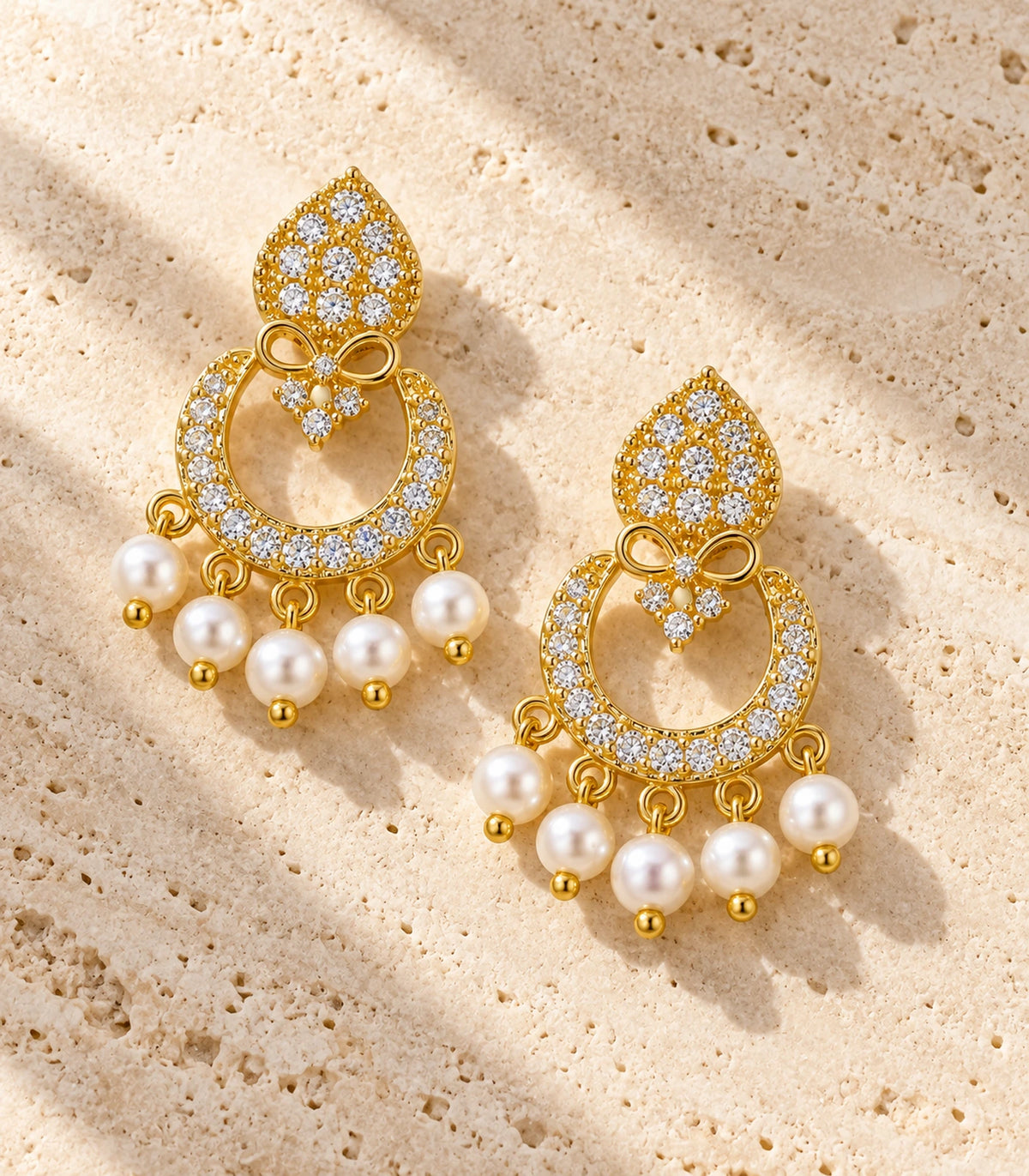 JIMIKI Gold-Tone Teardrop Bow Pearl Chandbali Earrings — pair in a styled flat lay #color_gold-tone / white