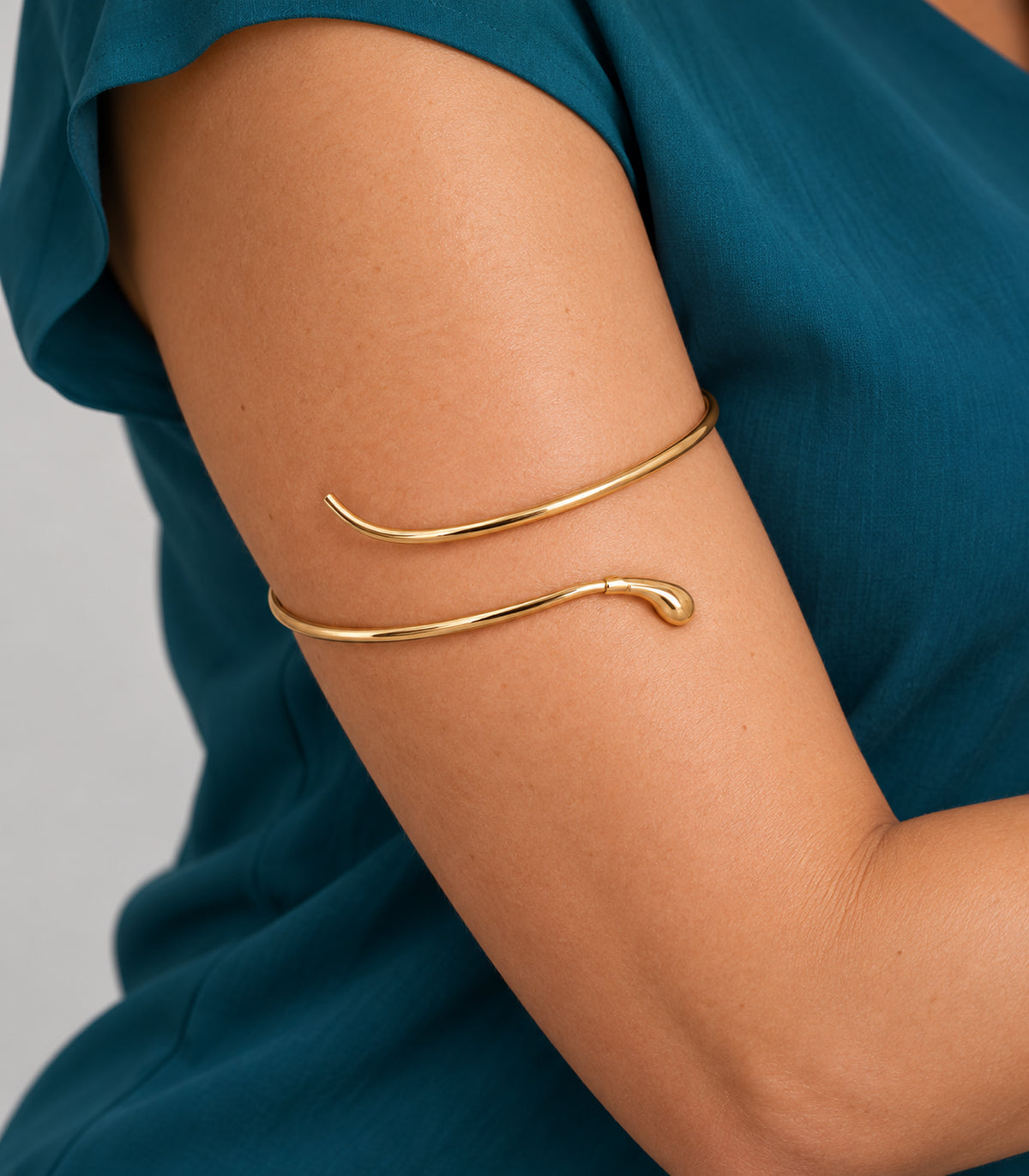 Closeup of the gold-tone arm cuff showing its teardrop tip and plain terminal on the upper arm