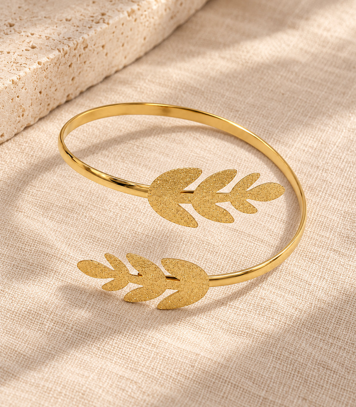 Complete gold-tone double leaf sprig arm cuff arranged on beige linen