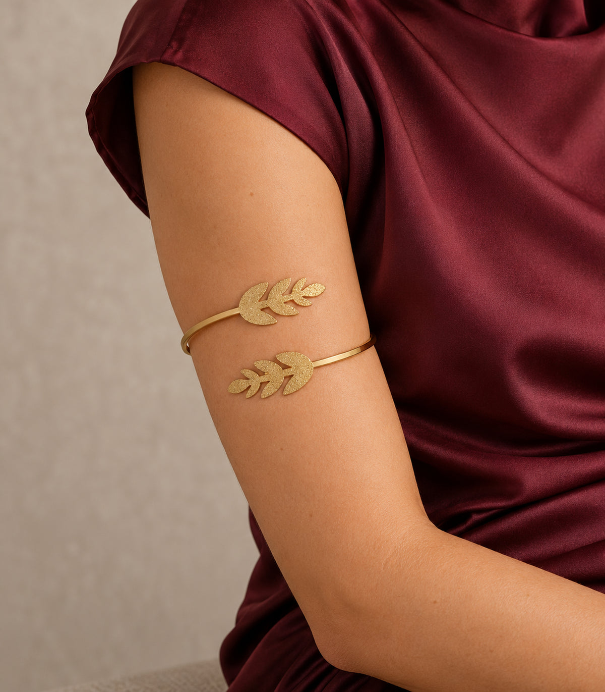 Gold-tone double leaf sprig cuff worn on the upper arm with burgundy clothing