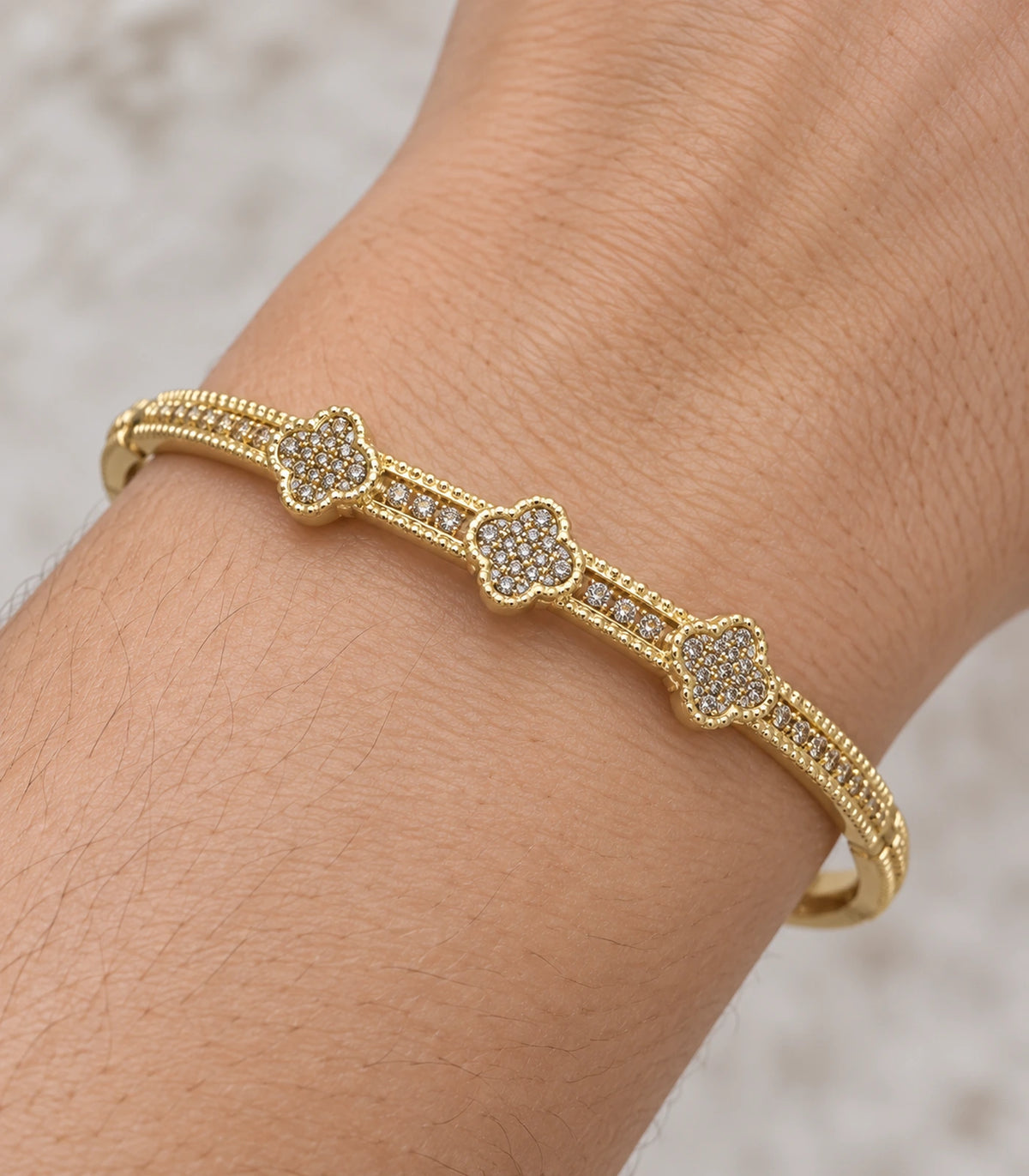 JIMIKI Gold-Tone Three Clover Pavé Bangle — close-up of the bangle worn on the wrist #color_gold-tone / clear
