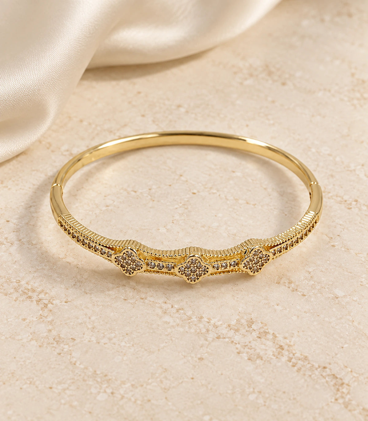 JIMIKI Gold-Tone Three Clover Pavé Bangle — bangle in a styled flat lay #color_gold-tone / clear