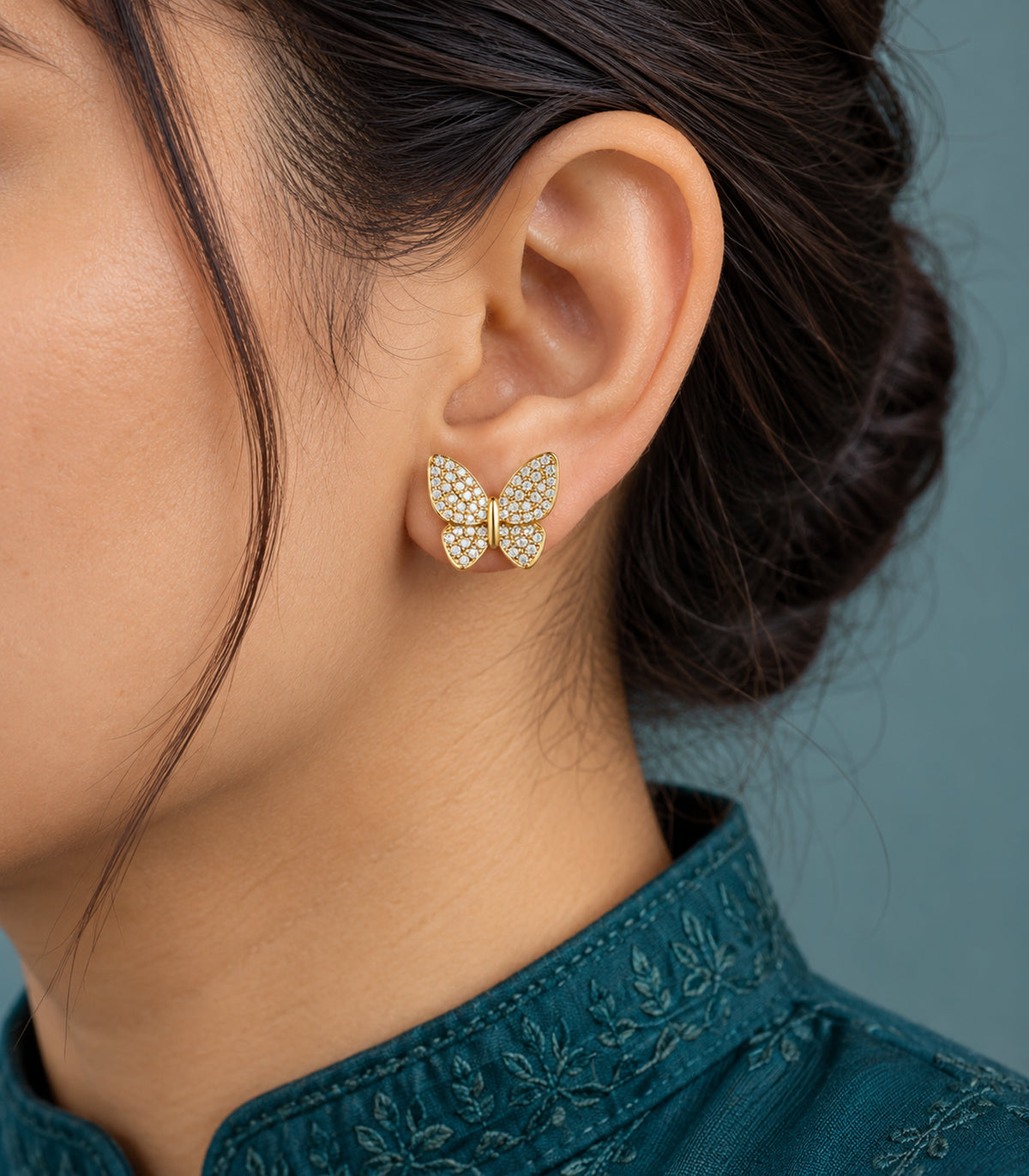 Close view of one four-wing pavé butterfly stud from the gold-tone earring set worn on an earlobe.