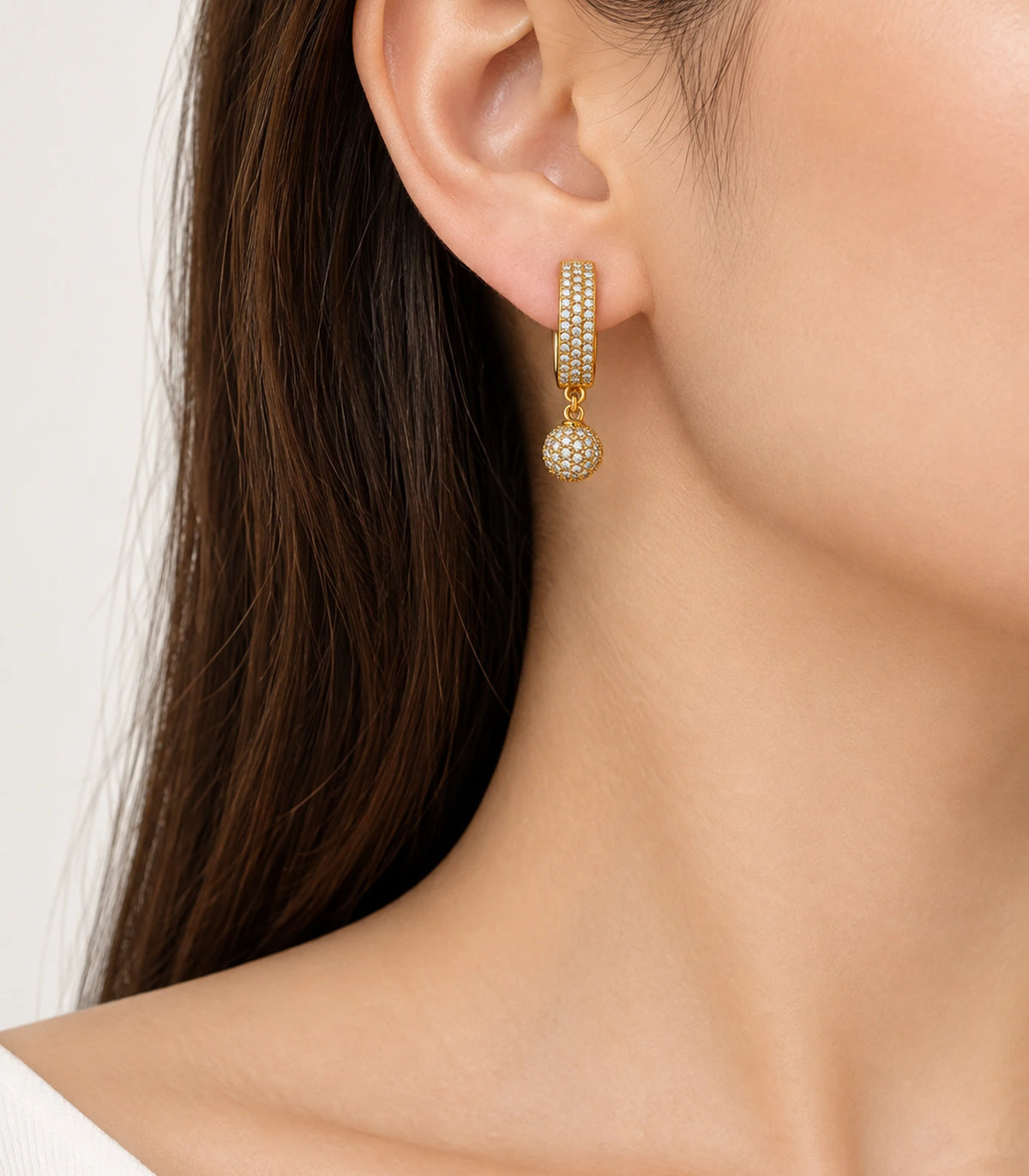 JIMIKI Gold-Tone Three-Row Pavé Ball Drop Huggie Earrings — worn on the ear #color_gold-tone / clear