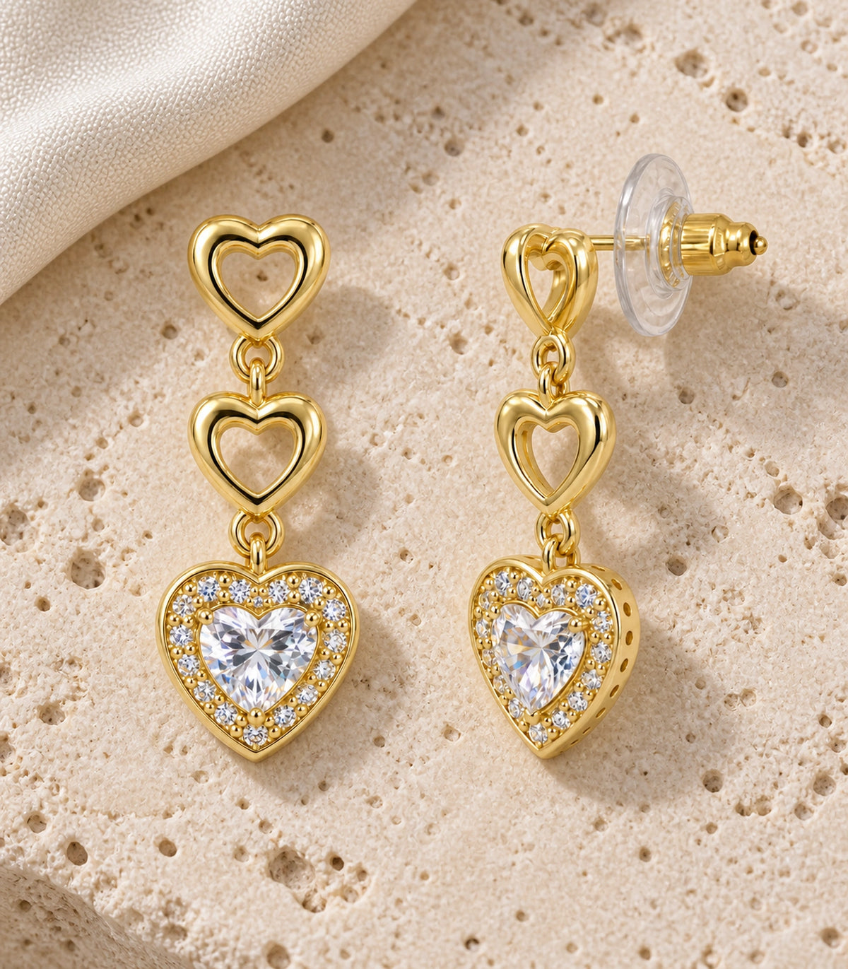 JIMIKI Triple Heart Crystal Drop Earring Pair in Gold tone / clear, editorial flat lay #color_gold tone / clear