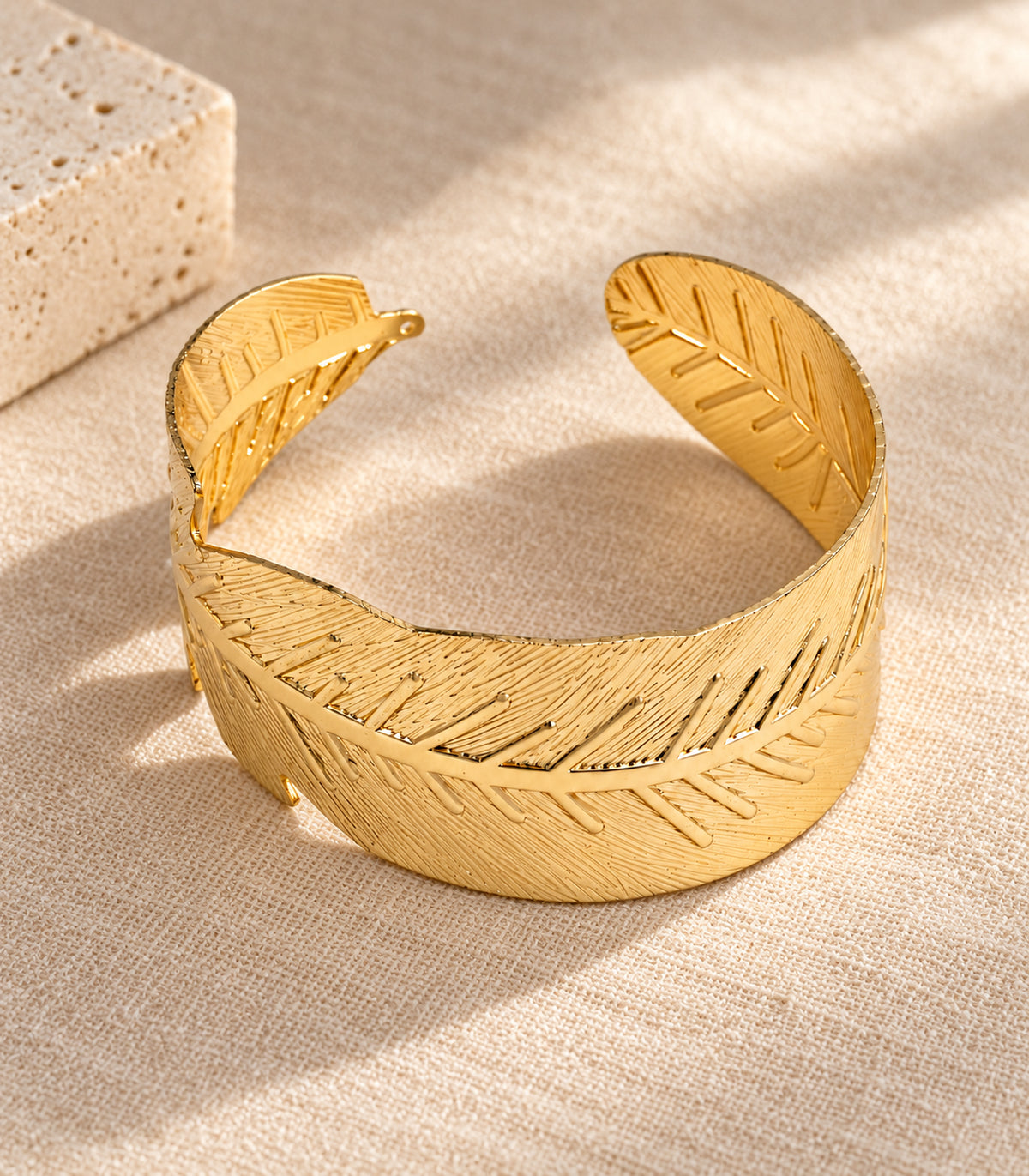Complete gold tone wide leaf arm cuff arranged on linen and stone