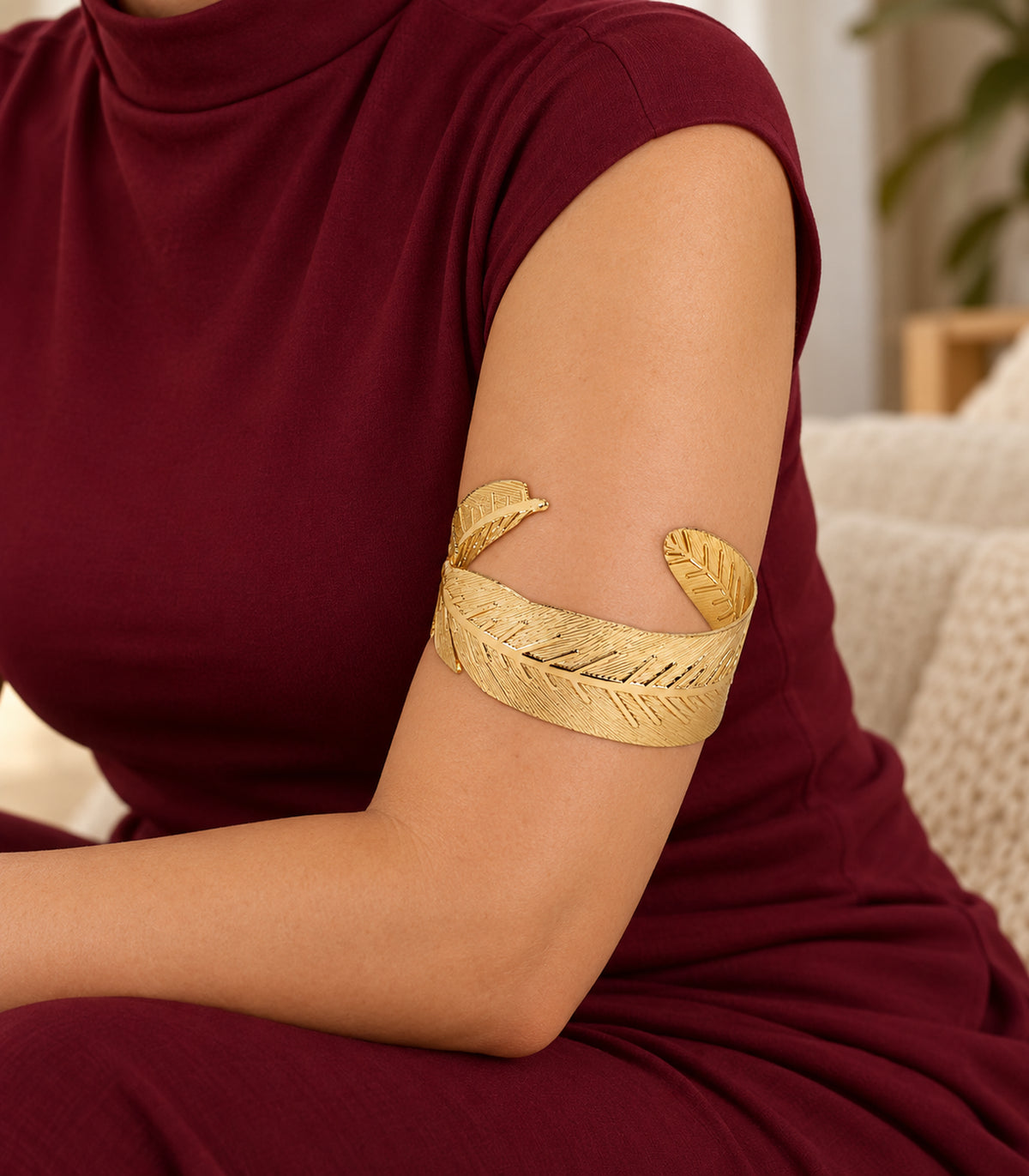 Gold tone wide leaf arm cuff worn on the upper arm with burgundy clothing