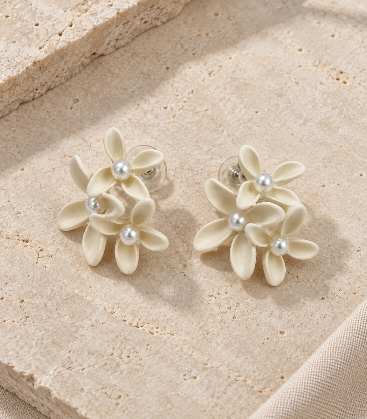 JIMIKI Ivory cascading floral cluster stud earrings, matching pair styled on a light textured surface #color_ivory
