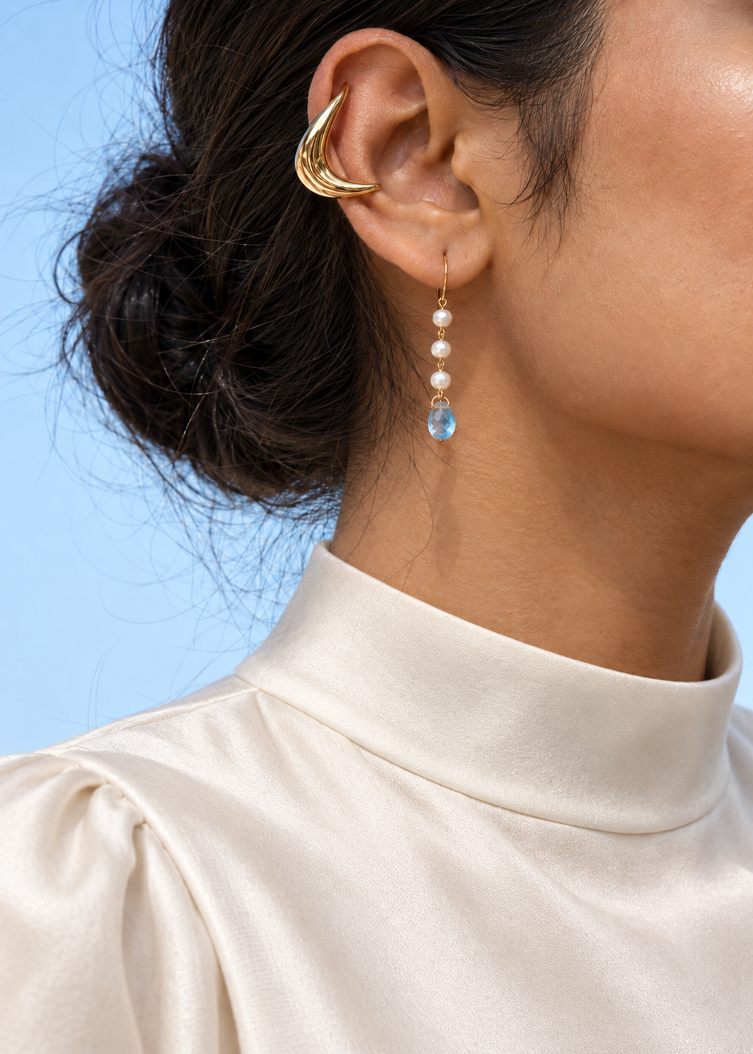 Close-up of pearl and blue drop earrings with an ivory high-neck silk blouse