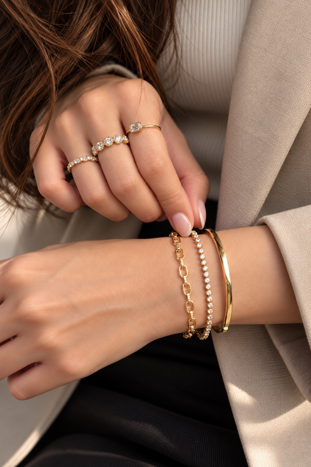 Delicate gold and crystal rings with layered bracelets styled with a beige blazer