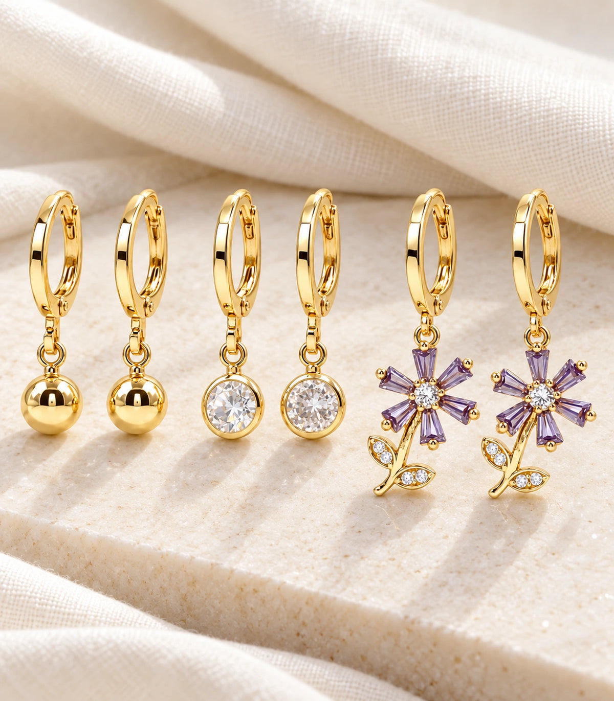 All six earrings of the gold-tone three-pair ball, crystal and purple flower set on ivory styling