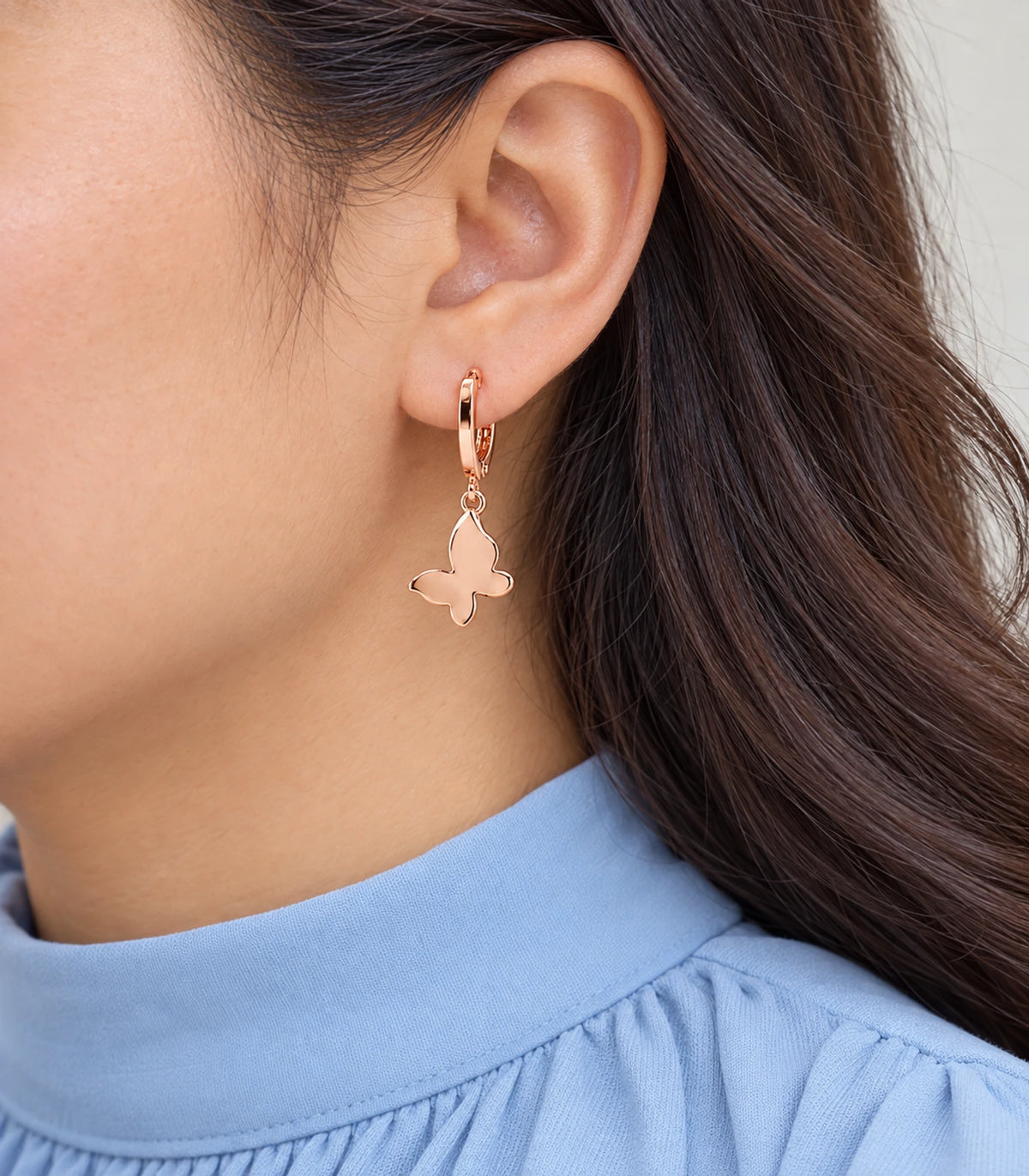 Closeup of a smooth rose gold tone butterfly hoop earring from the three-pair set