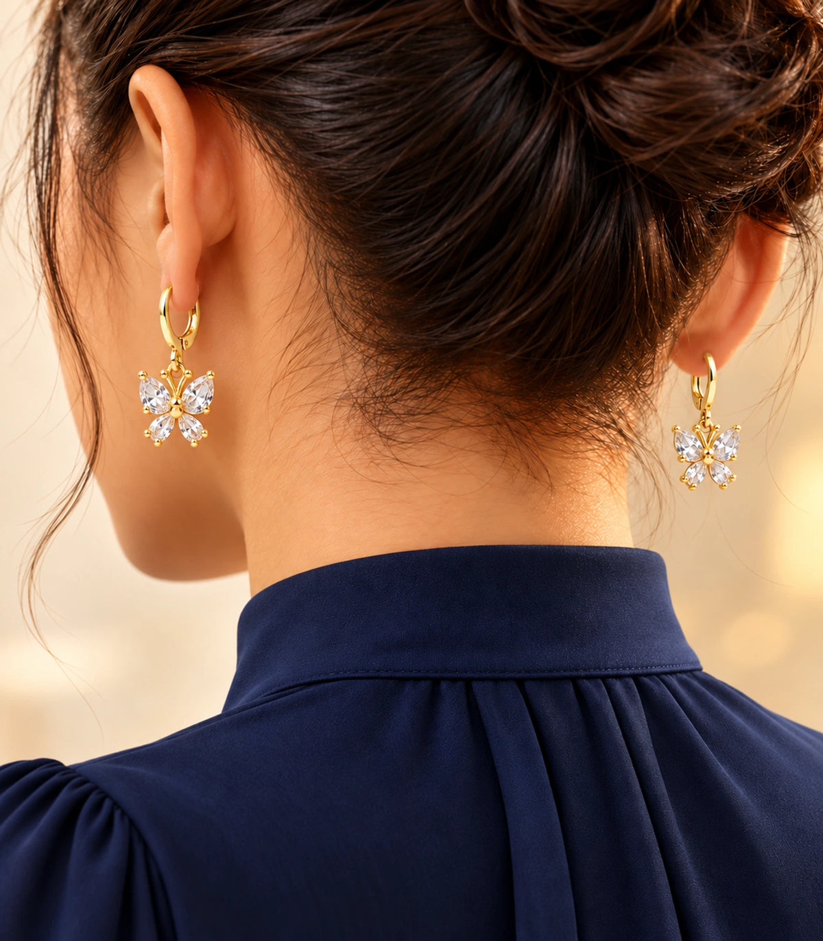 Gold-tone crystal butterfly hoop earrings styled with a navy high-neck blouse