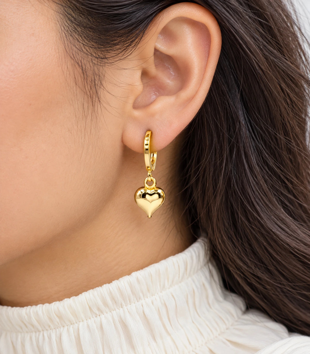 Gold-tone puffed heart hoop earring worn closeup