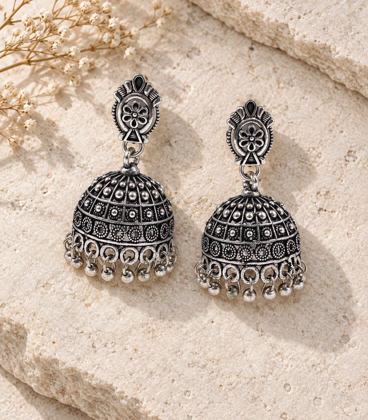JIMIKI Oxidized Silver Oval Flower Grid Dome Jhumka Earrings - styled flatlay of the matching earrings #color_oxidized-silver