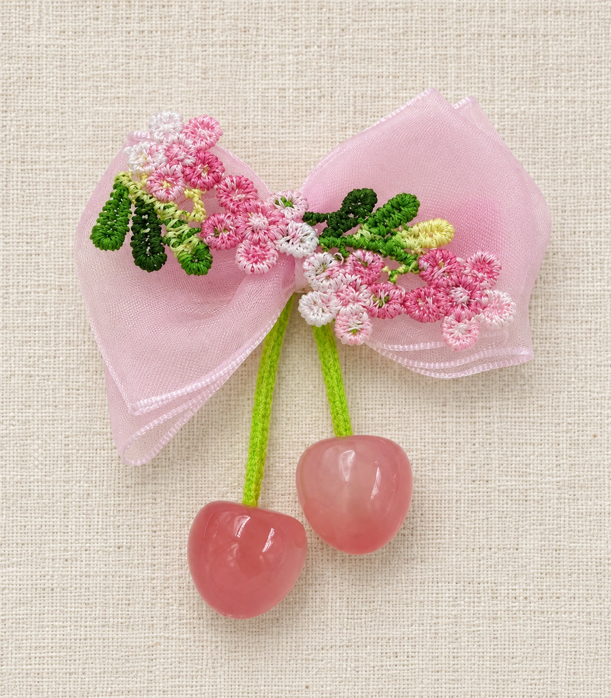 JIMIKI Pink Embroidered Bow Hair Clip with Cherry Charms in Pink, editorial flat lay