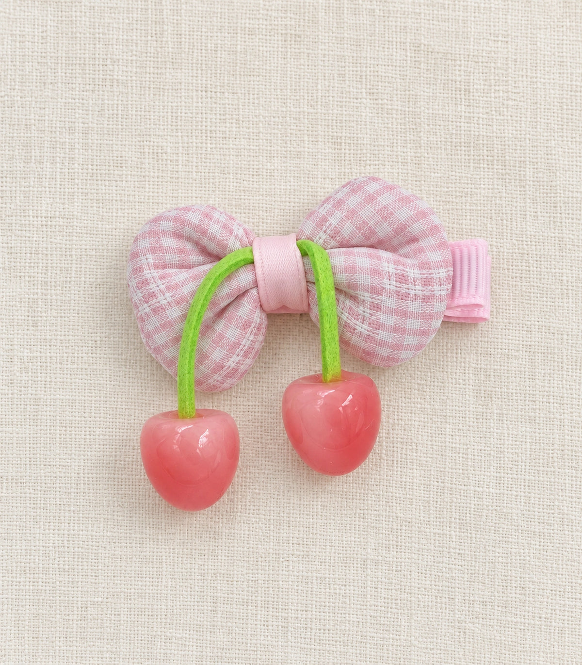 JIMIKI Pink Gingham Bow Hair Clip with Cherry Charms in Pink, editorial flat lay