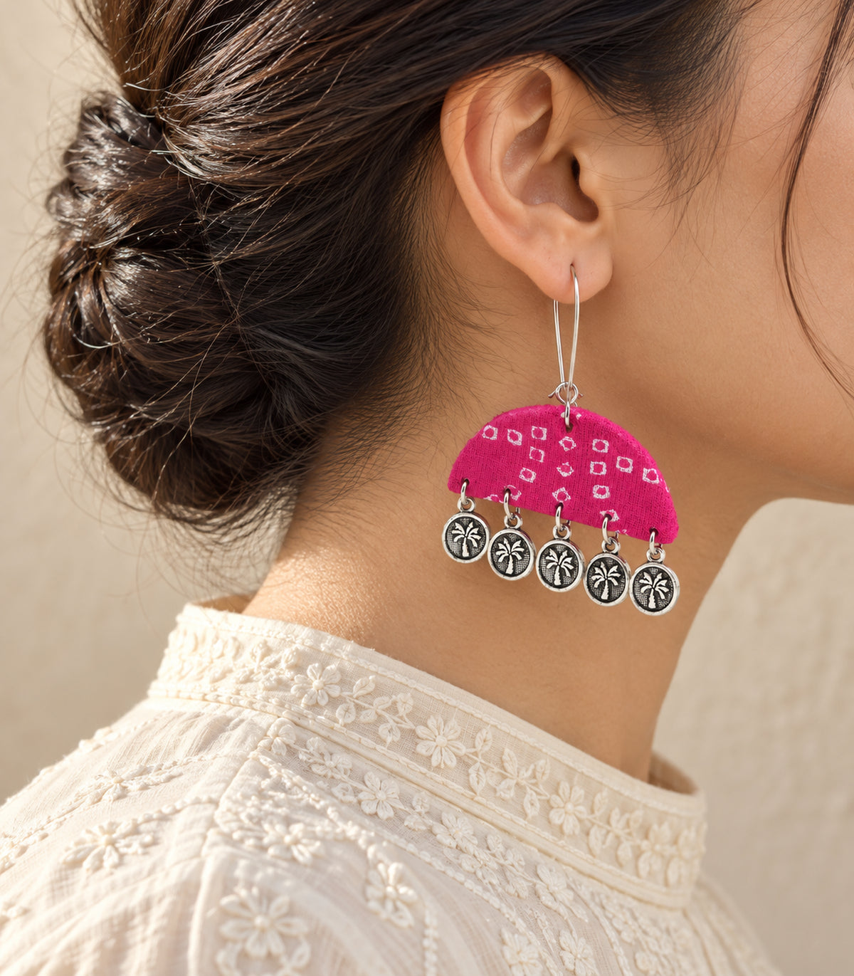 Pink semicircle five-coin earring worn with ivory clothing, rear three-quarter view