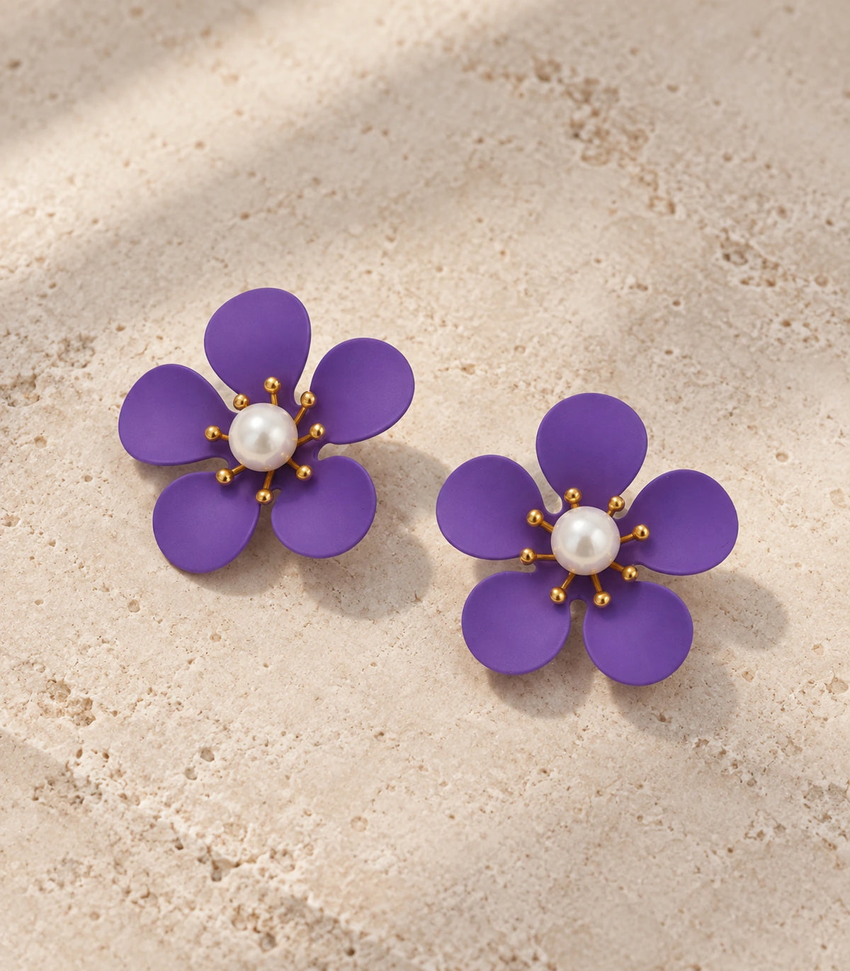 JIMIKI purple five-petal flower stud earrings with pearl-effect centre, matching flower stud pair in an editorial flat lay #color_purple