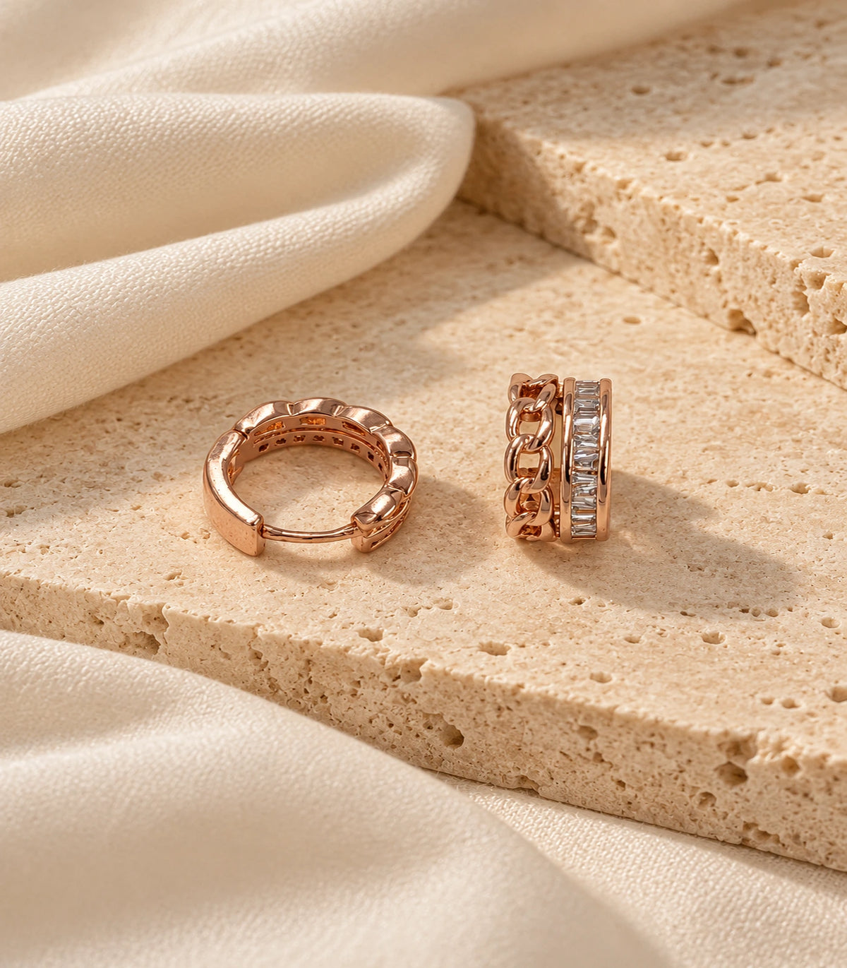 JIMIKI rose gold baguette chain double row huggie earrings, pair styled on textured stone #color_rose-gold-tone