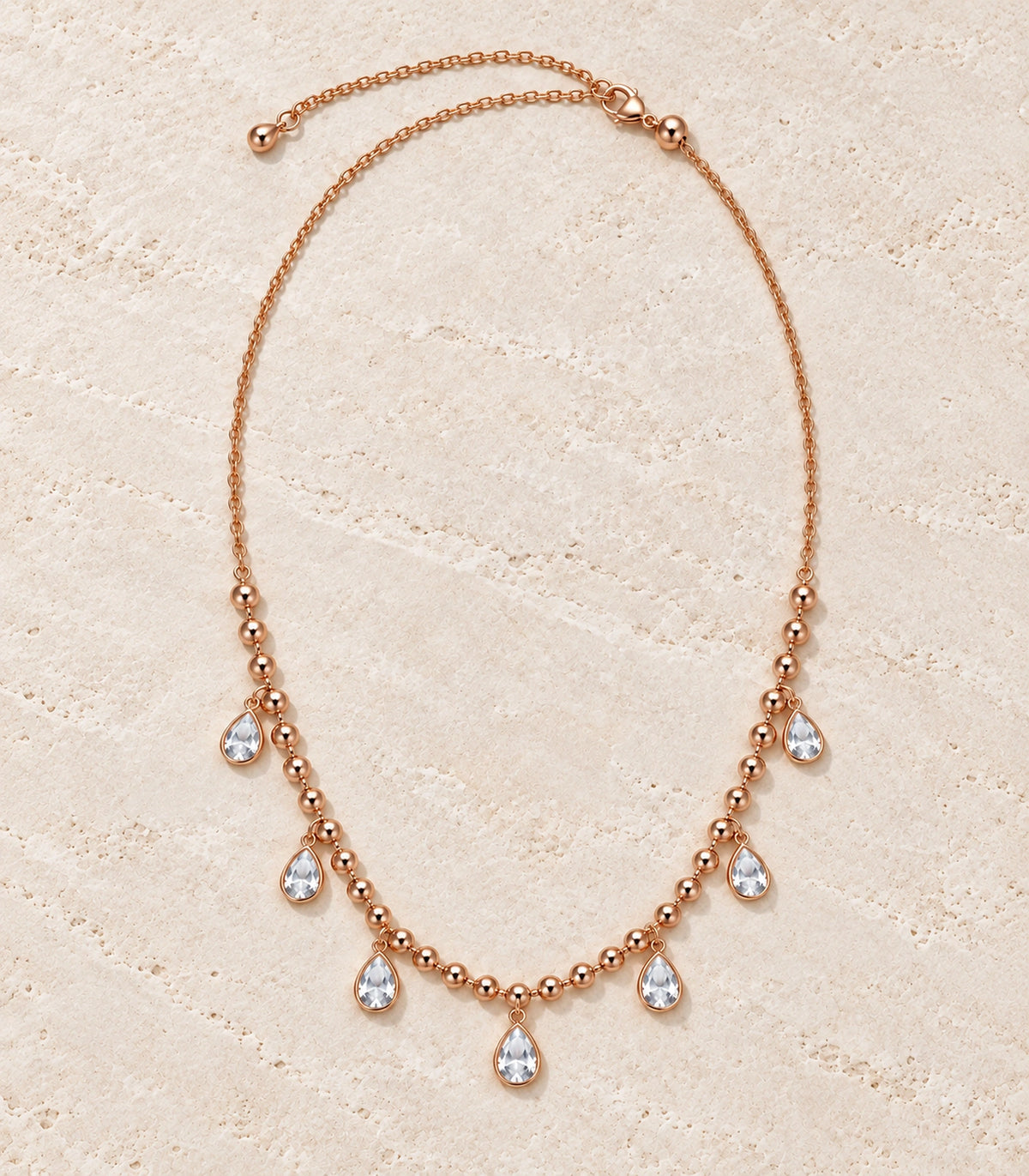 JIMIKI Rose-Gold Bead and Pear-Crystal Drop Necklace in Rose Gold - editorial flatlay #color_rose-gold
