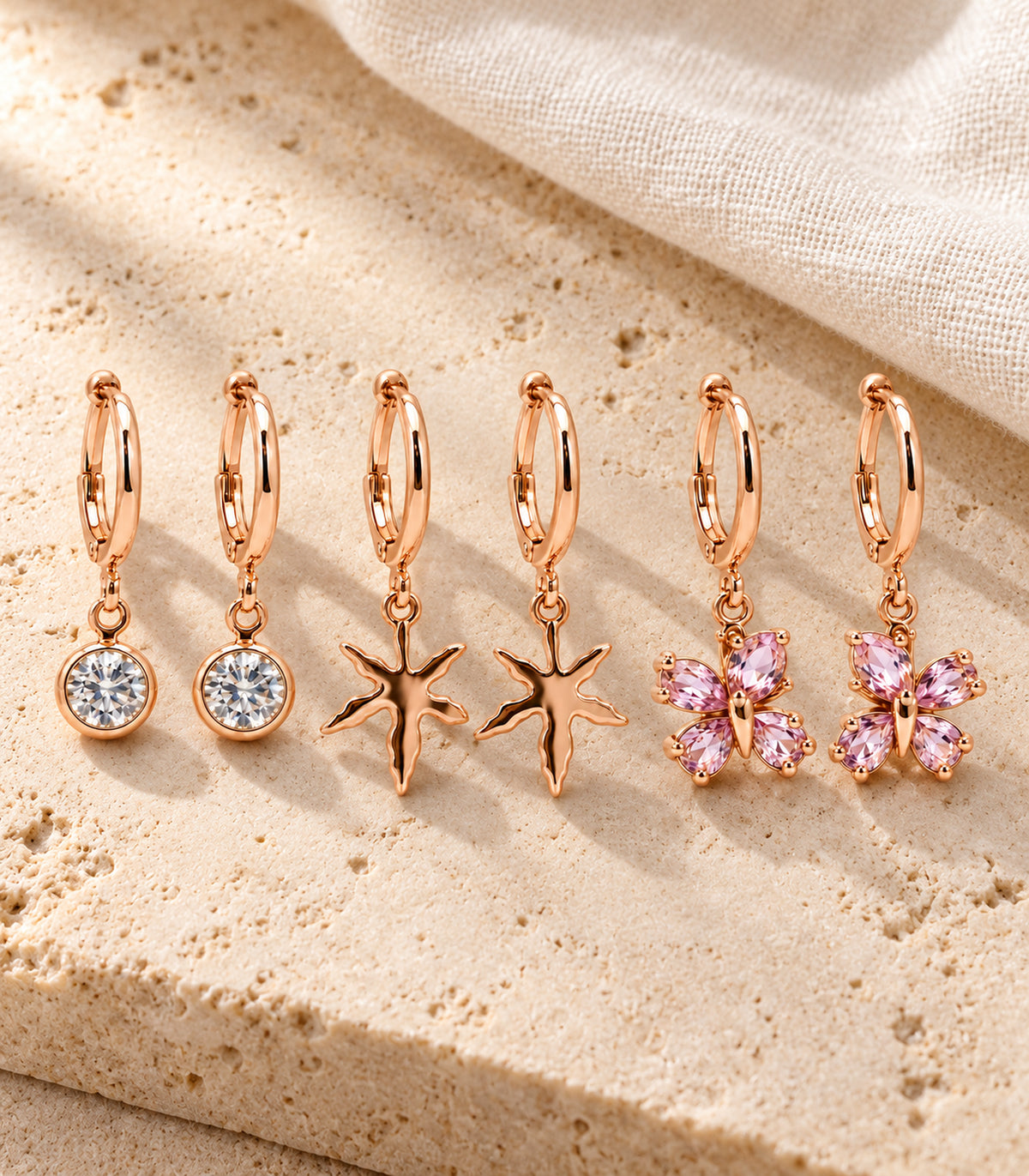 Complete three-pair rose gold tone crystal, starfish and pink butterfly hoop set on pale stone