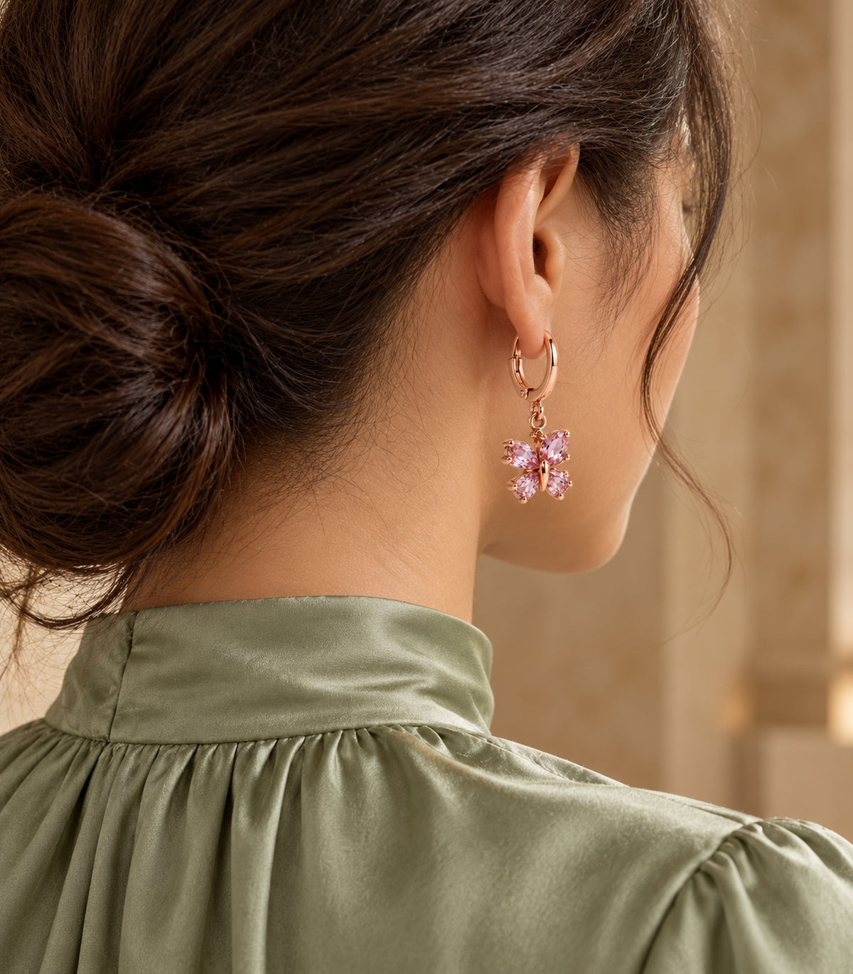 Rose gold tone four-stone pink butterfly hoop earring worn in a rear three-quarter view