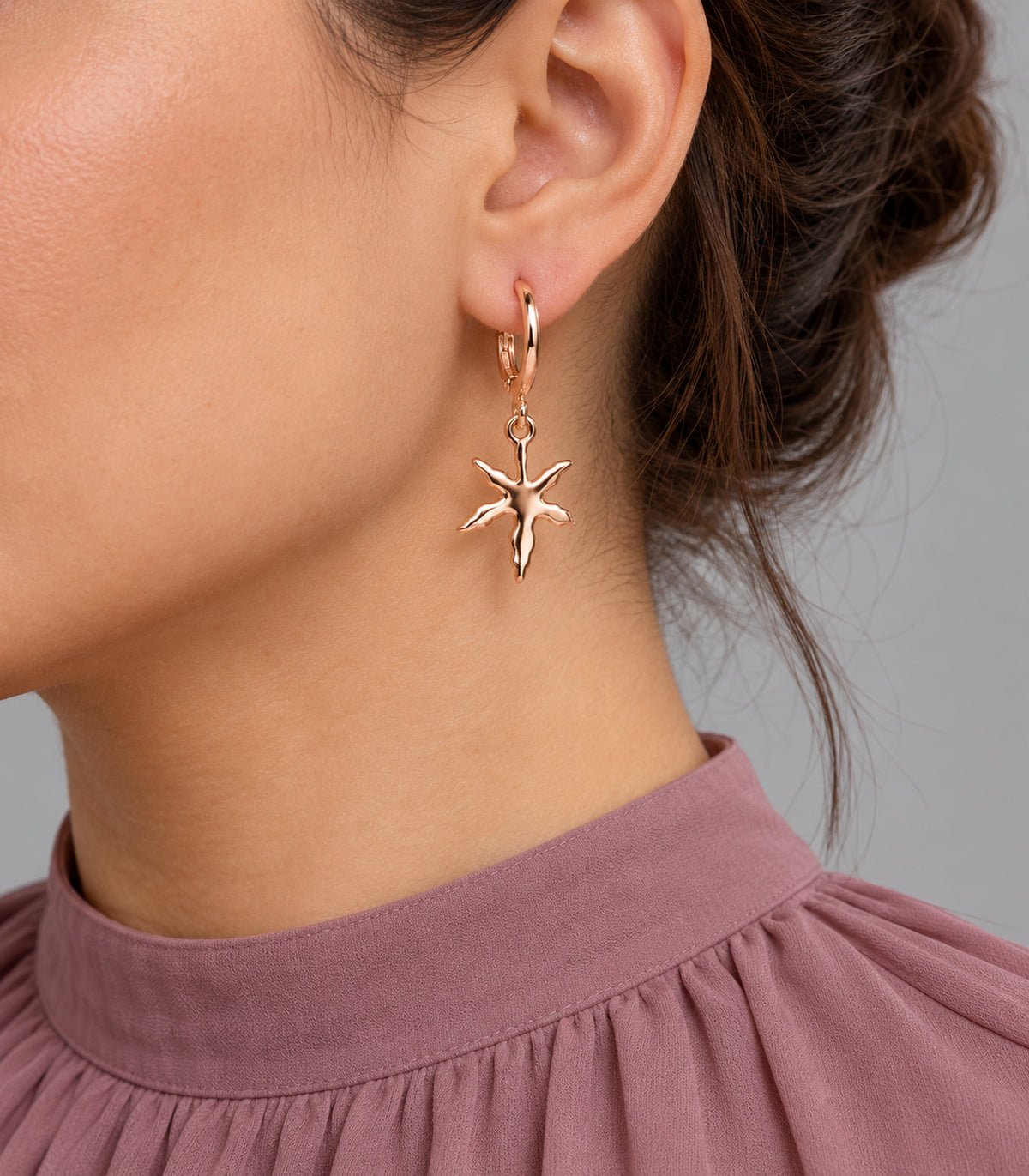 Rose gold tone five-arm starfish hoop earring worn on one ear