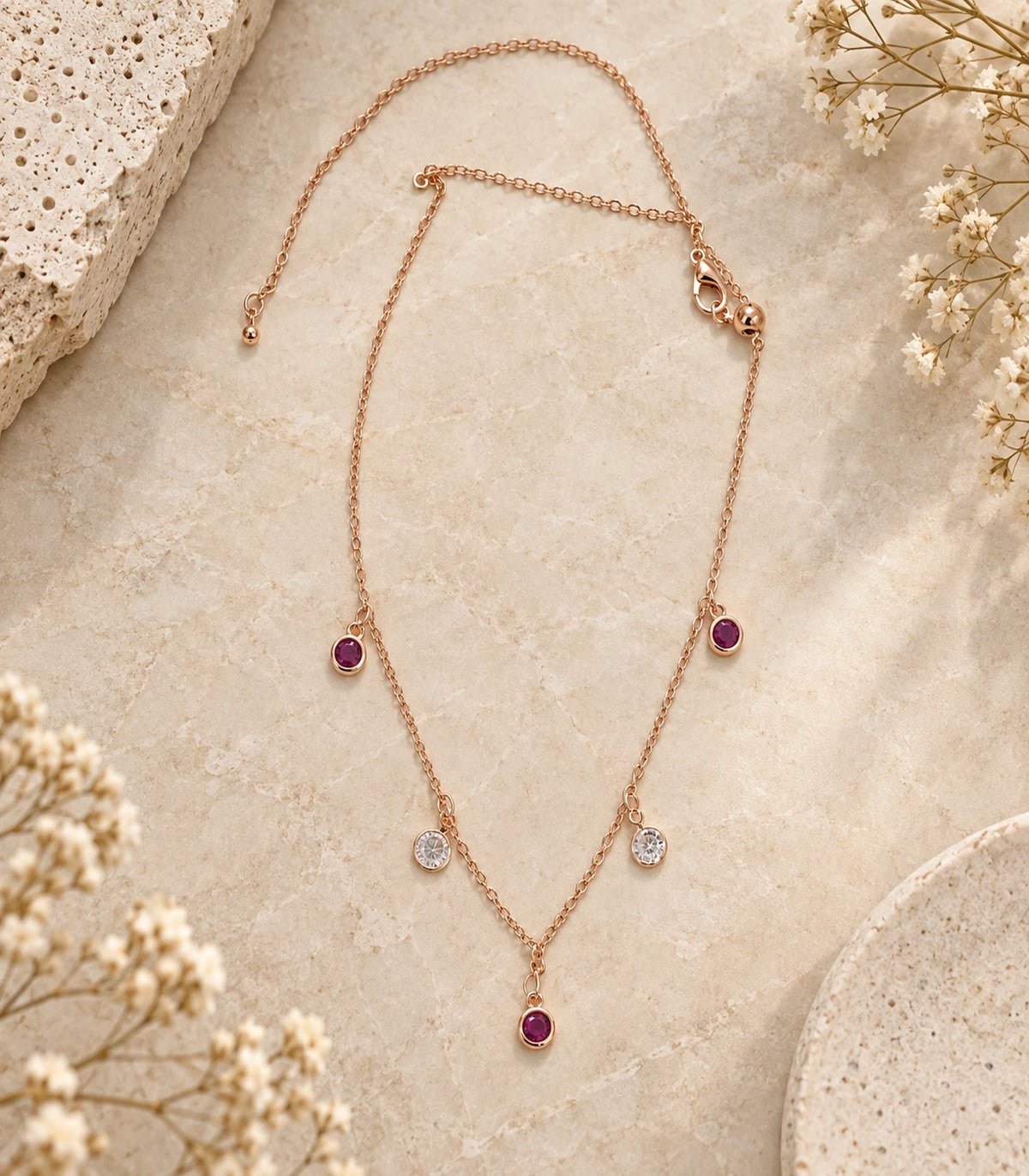 JIMIKI Purple and Clear Five-Stone Station Necklace in rose-gold tone, necklace arranged on a pale textured surface #color_purple & clear