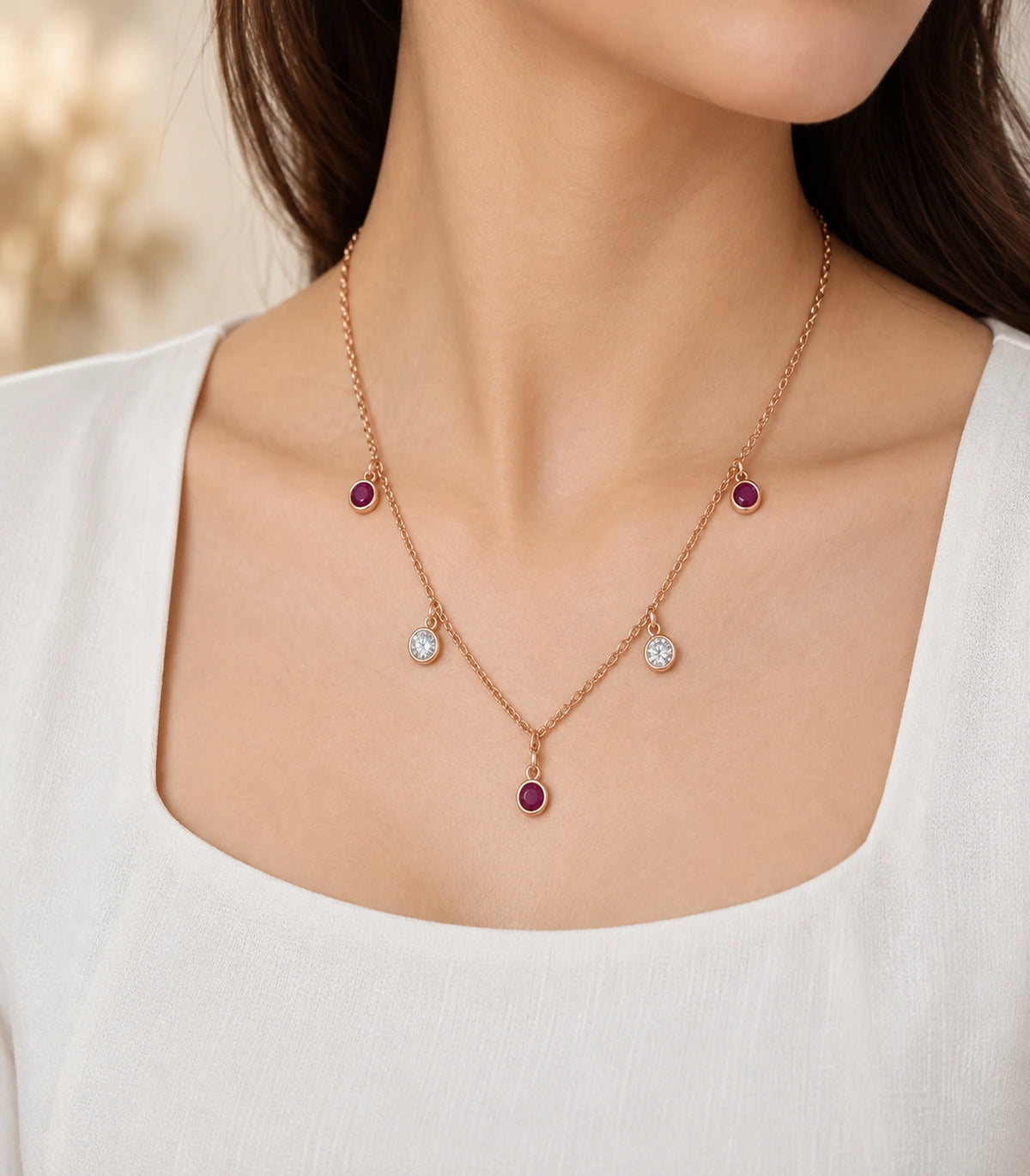 JIMIKI Purple and Clear Five-Stone Station Necklace in rose-gold tone, necklace worn with a cream top in warm light #color_purple & clear