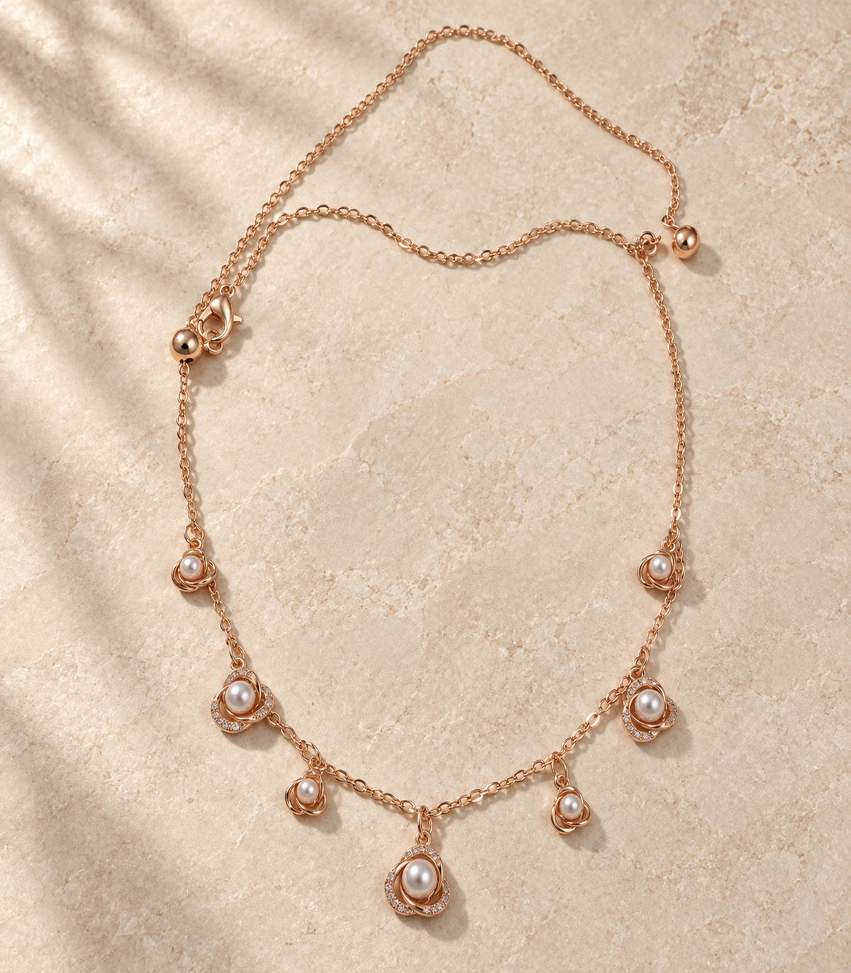JIMIKI Rose Gold pearly rose charm necklace, complete necklace arranged on a pale textured surface #color_rose gold