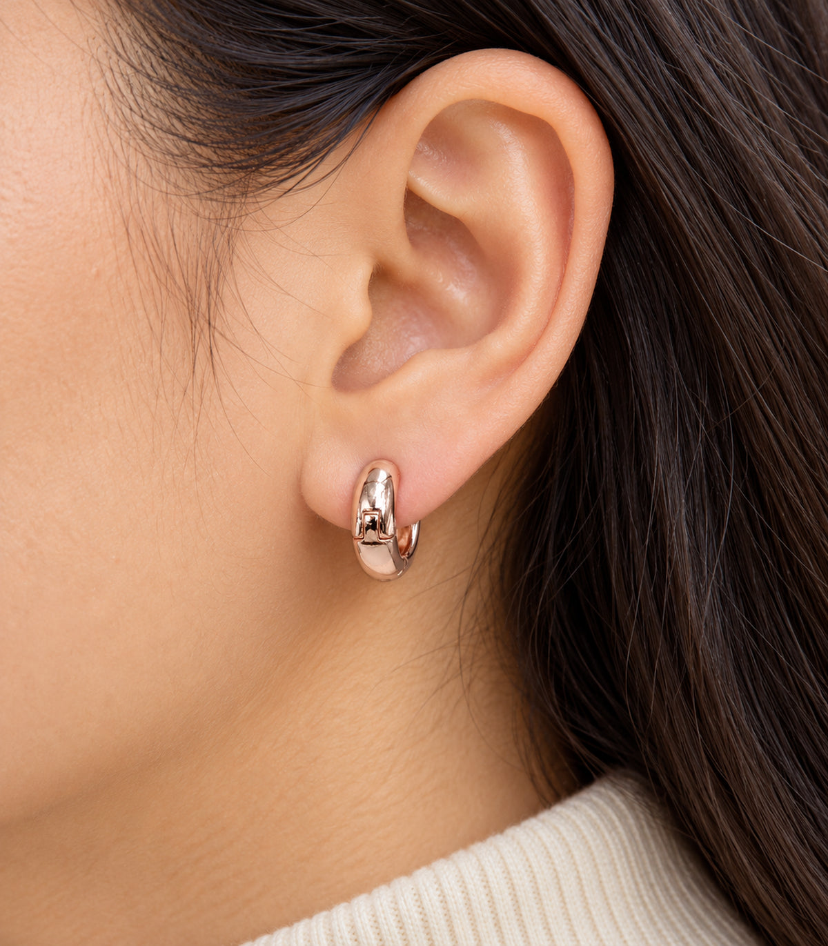 Close-up of a rose-gold-tone smooth chunky hoop earring worn on an ear.