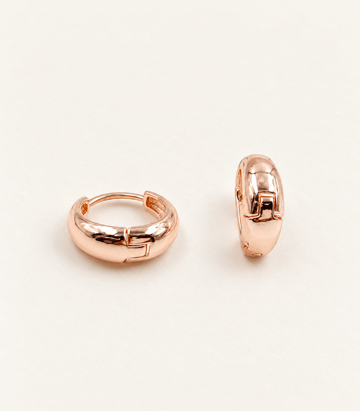 Rose-gold-tone smooth chunky hoop earring pair in an editorial flat lay.