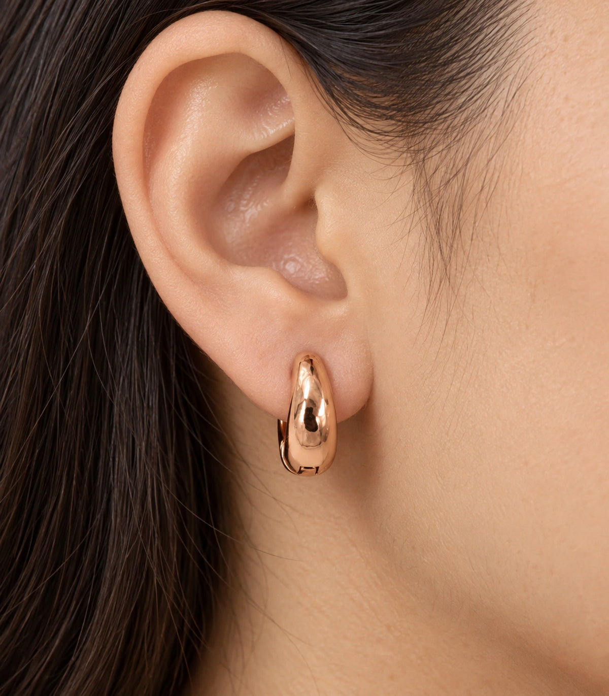 JIMIKI Smooth Tapered Huggie Earrings in Rose Gold Tone — worn close-up detail #color_rose-gold-tone