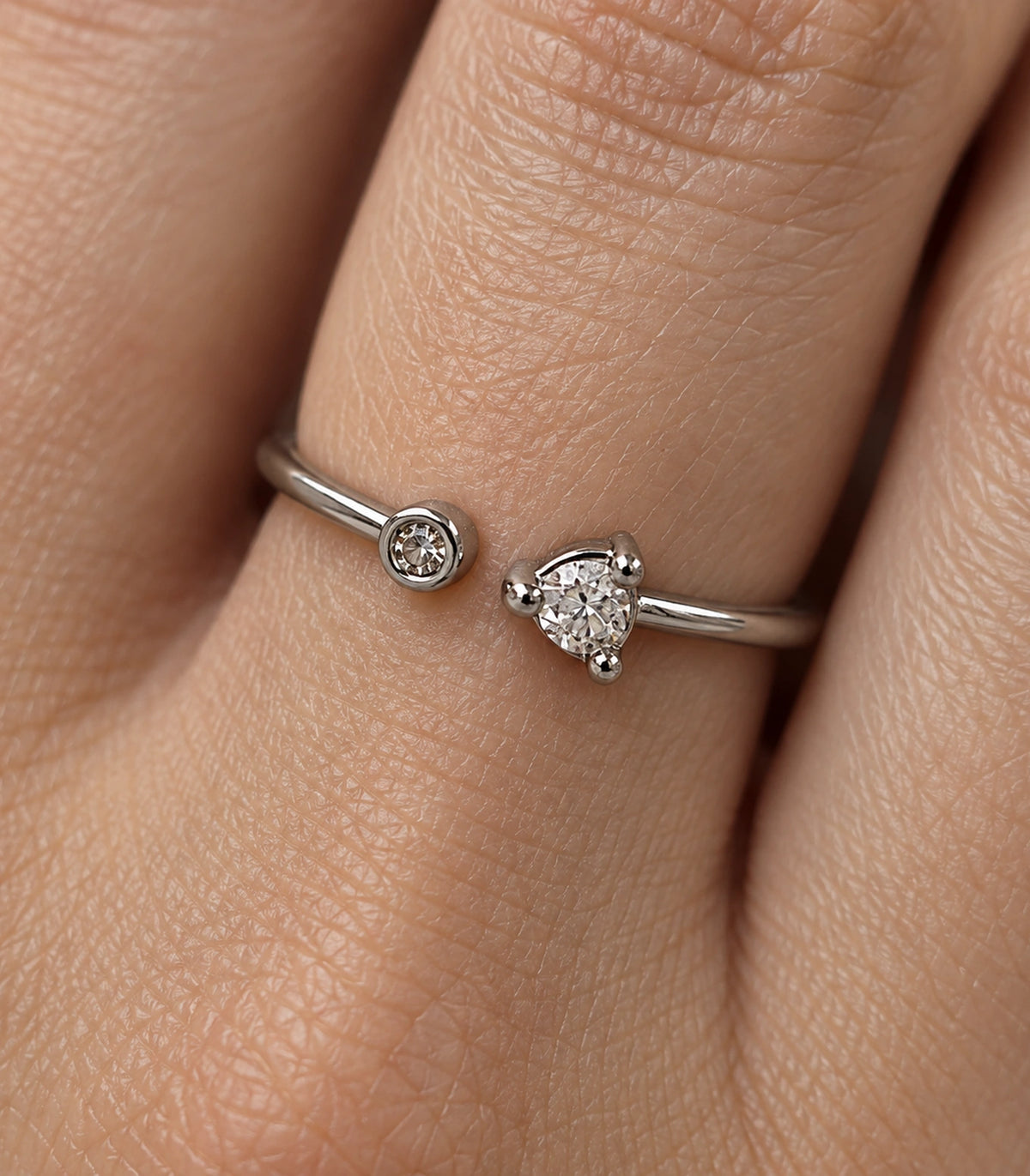 Close-up of the worn ring showing its unequal clear round accents, bezel and three-prong settings