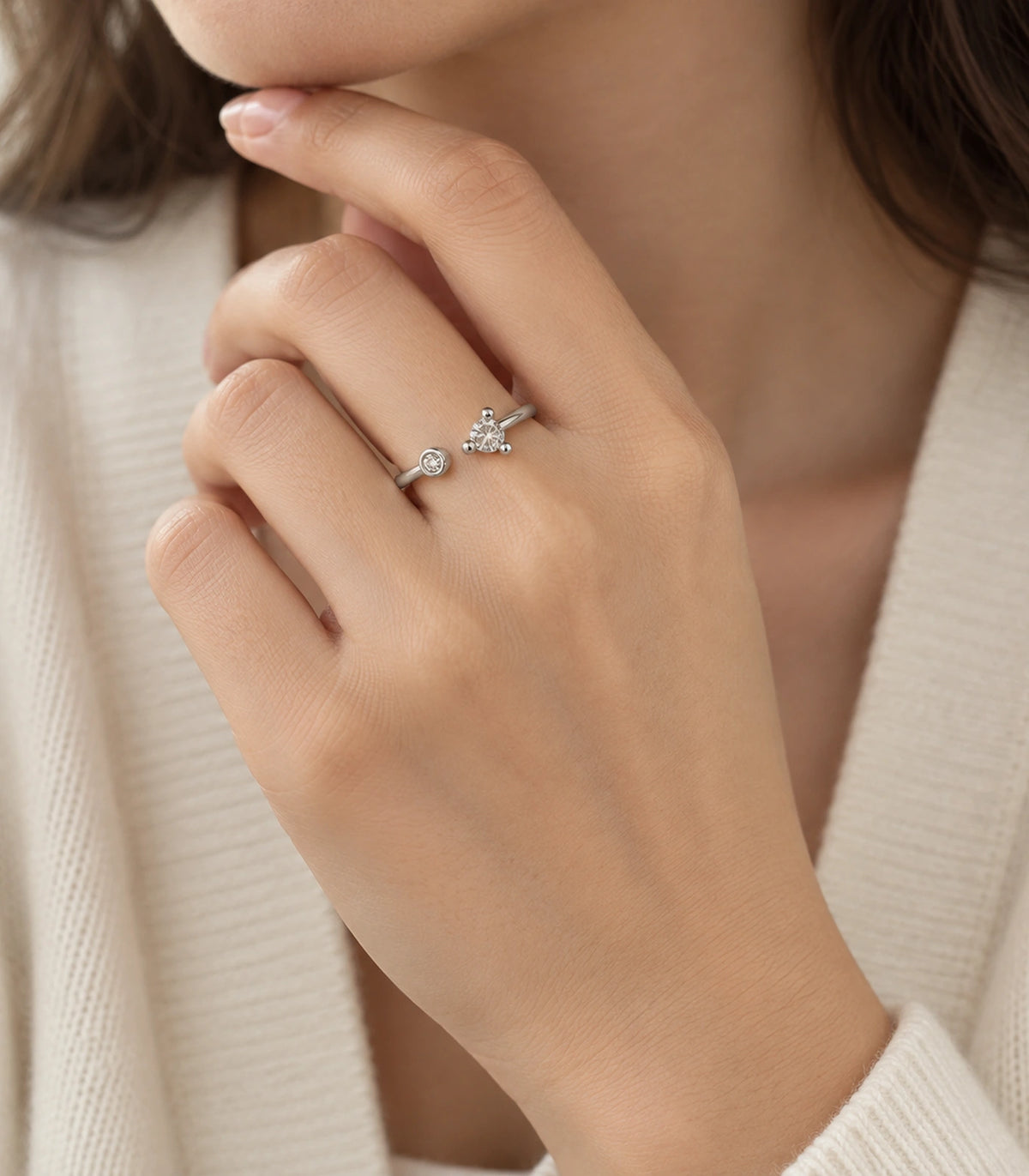 Silver-tone asymmetric open ring worn in a hand-near-chin pose with cream clothing