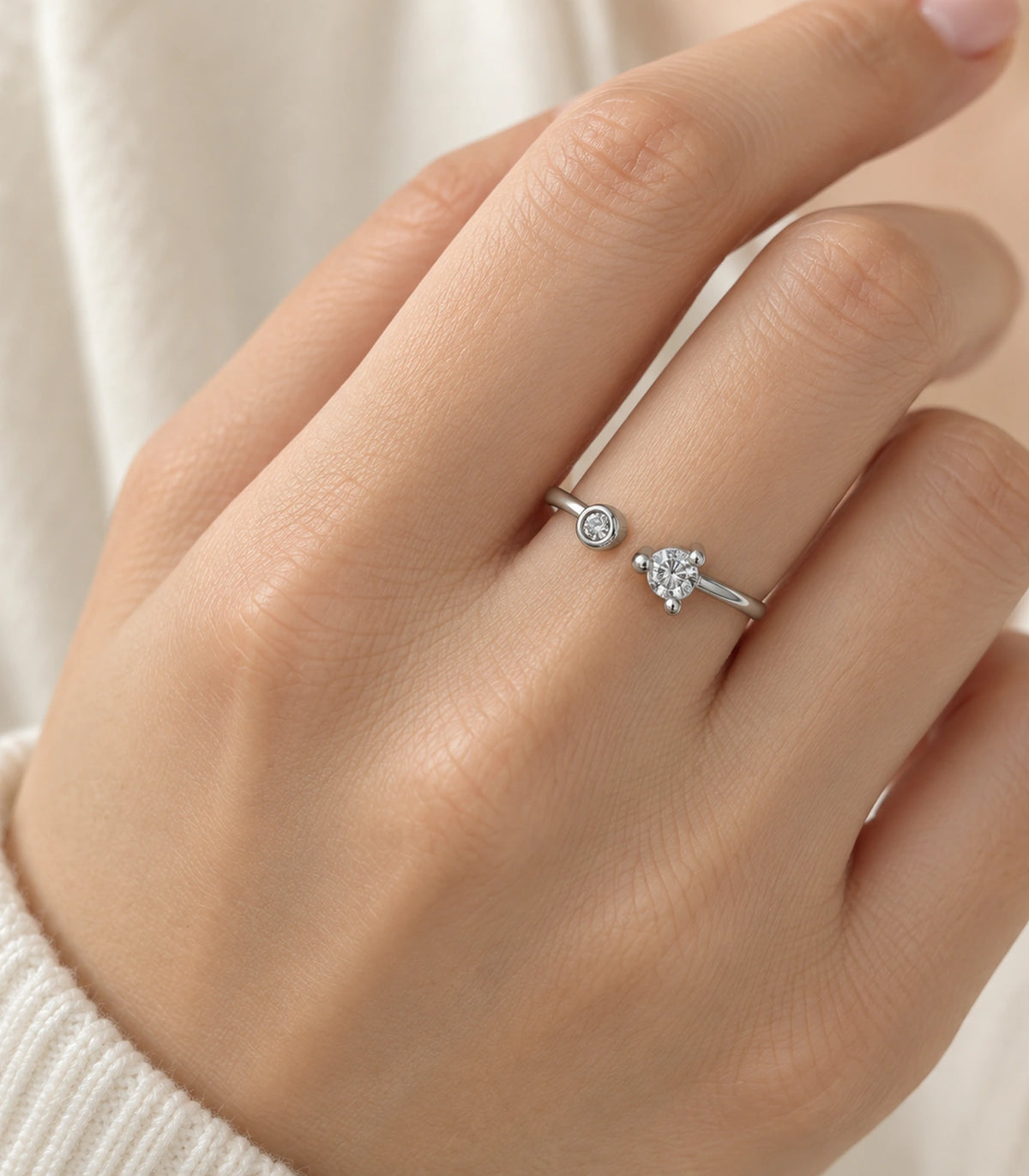 Silver-tone two-crystal-style open ring worn on a finger with a cream knit sleeve